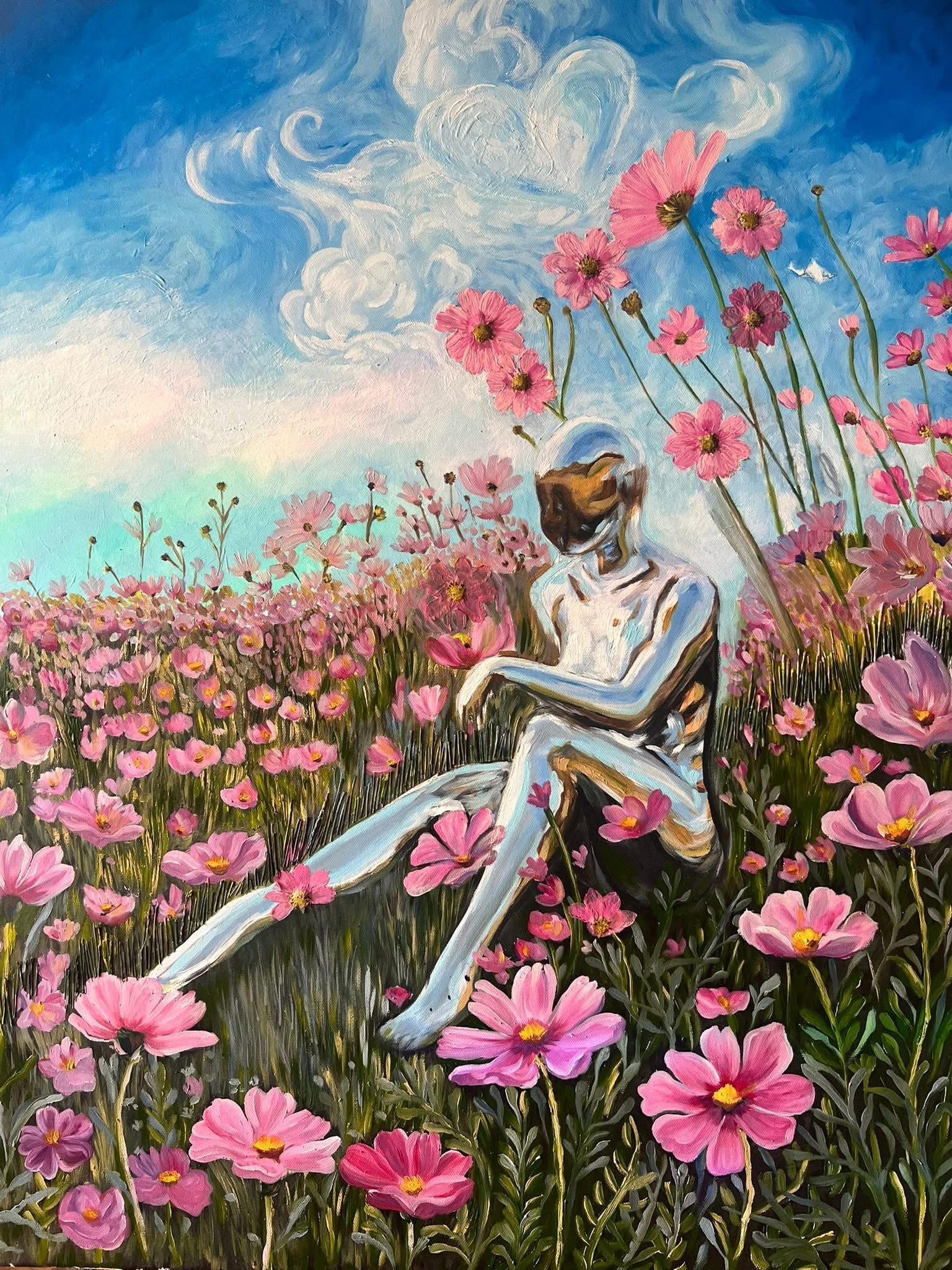 A person with a cat mask sitting among pink flowers in a field under a blue sky with clouds.