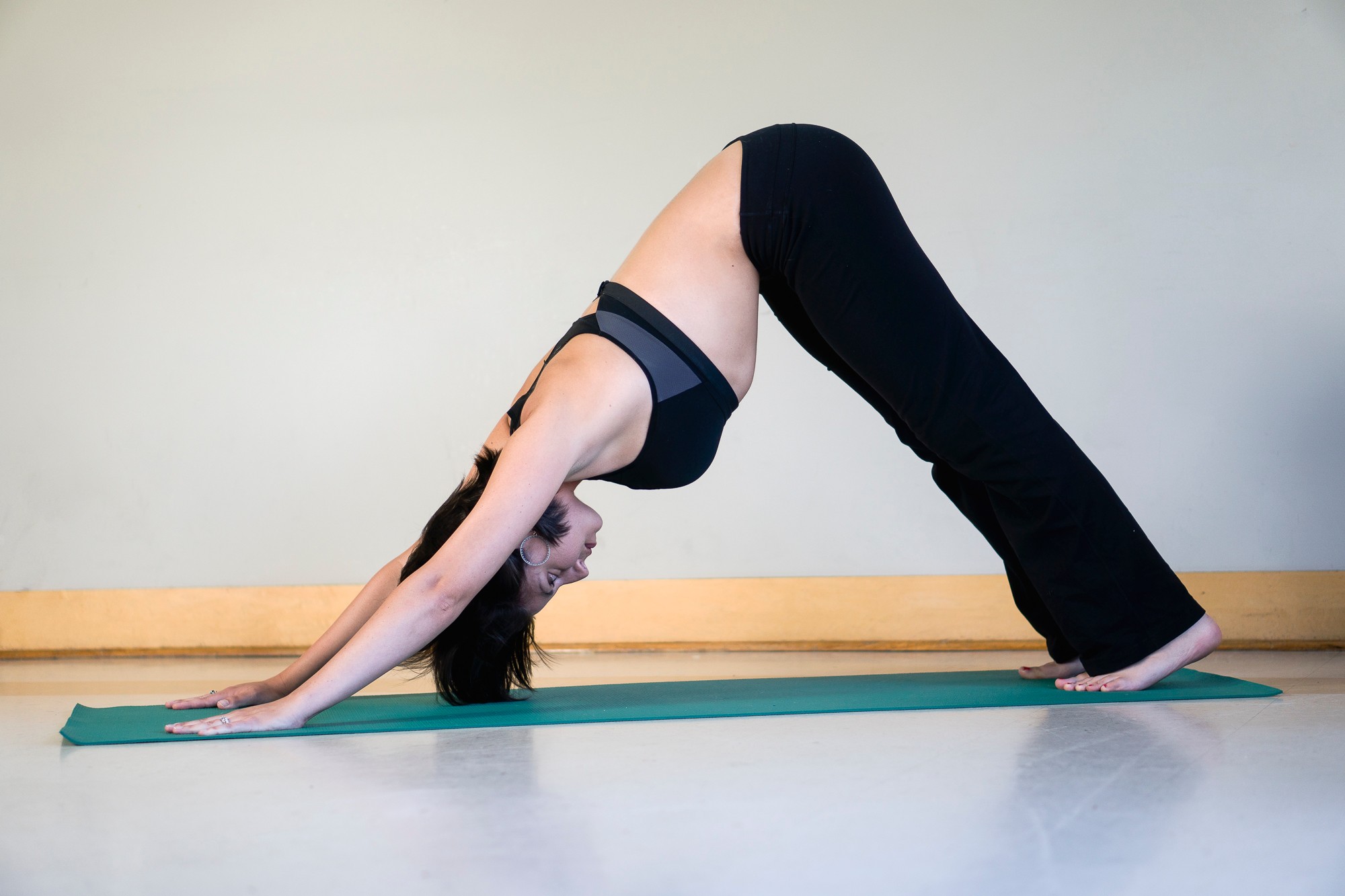 Person performing downward dog yoga pose on a mat, with hands and feet on the floor, hips raised, head between arms.