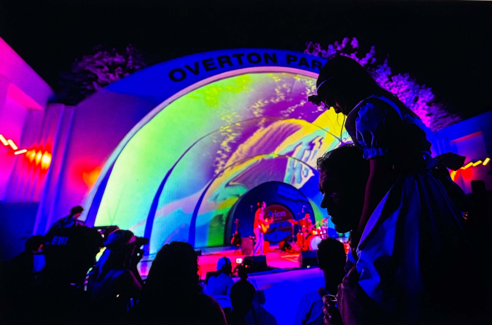 Silhouettes of people in front of a colorful stage with a rainbow arch and the text 'Overtorn Park'.