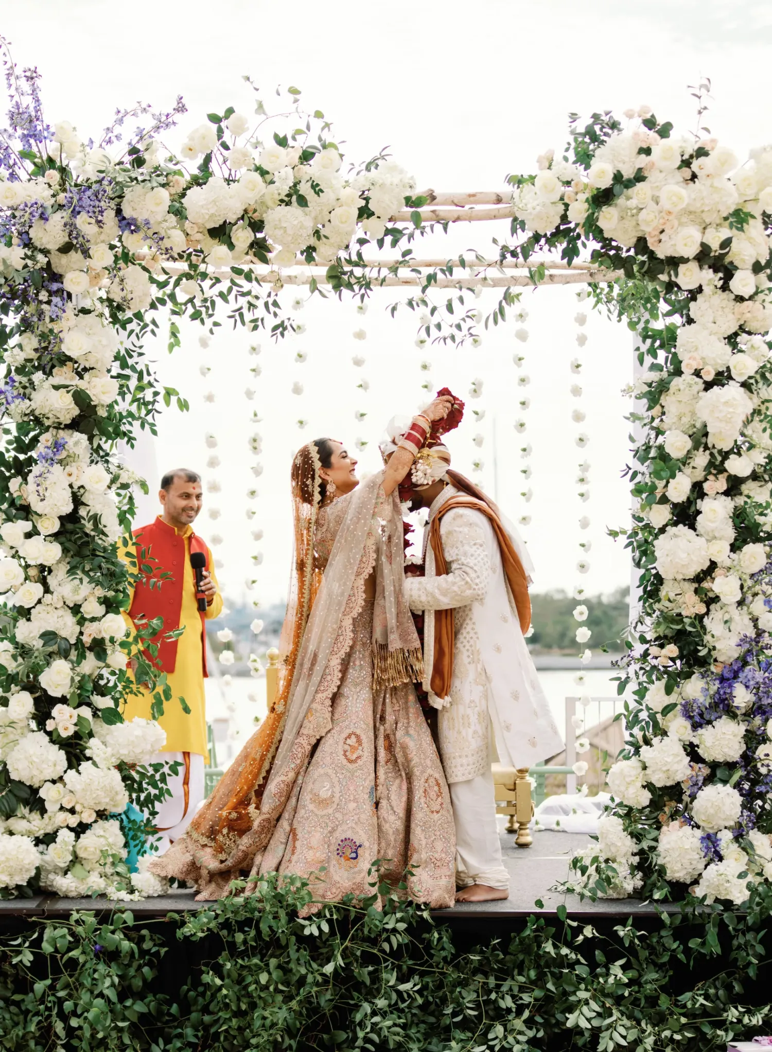 Bride and groom kissing under floral arch at outdoor wedding, with a person in yellow in the background.