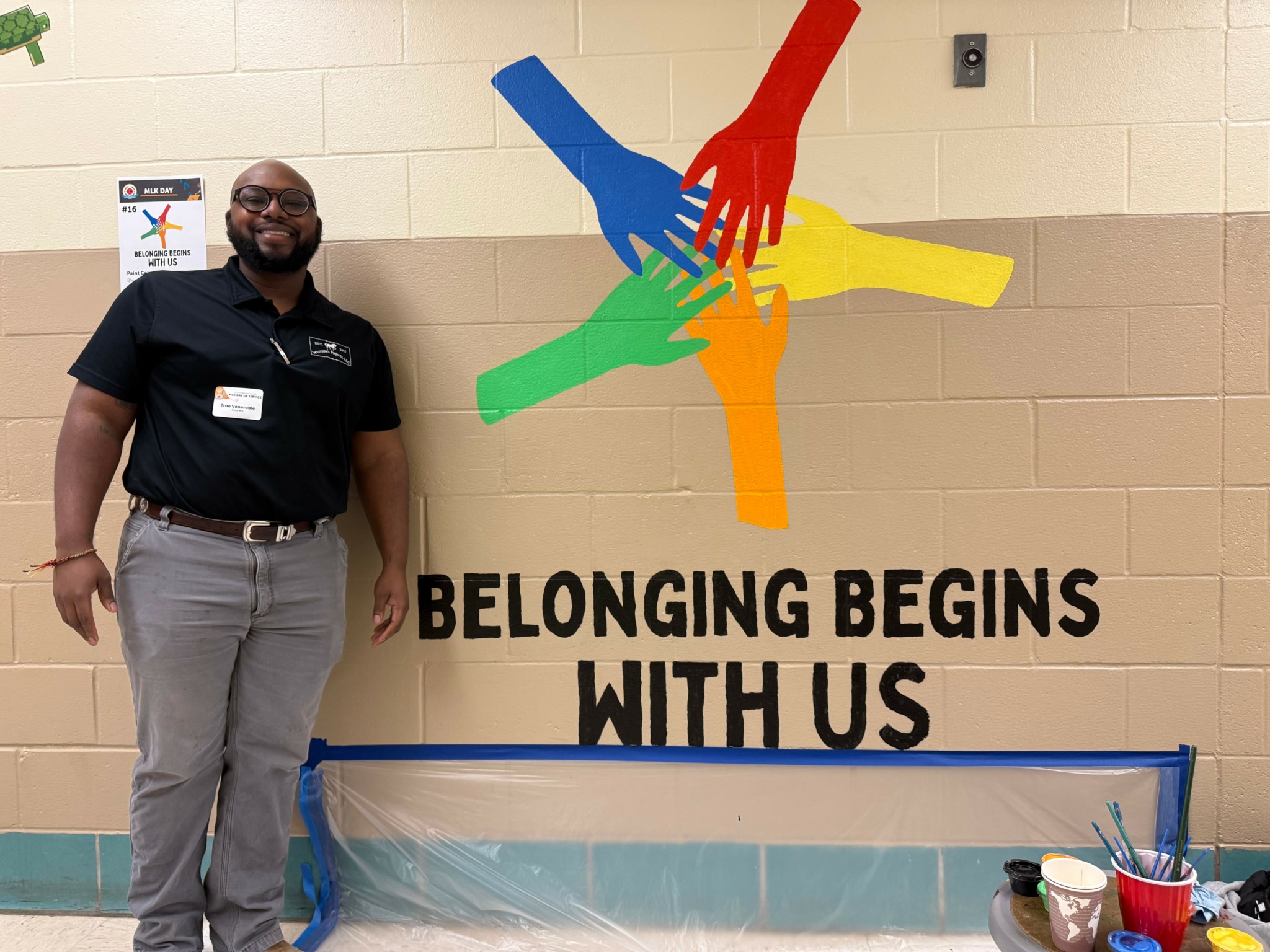 Man standing next to a wall with a colorful hand graphic and the text 