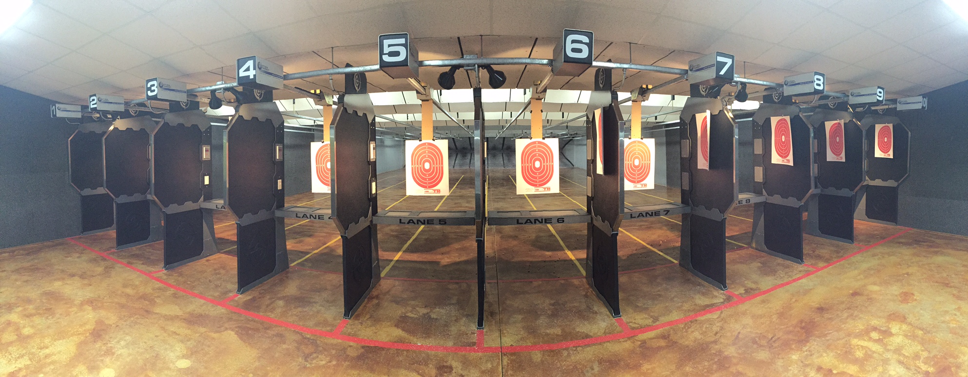 Indoor shooting range with numbered targets and black barriers, red lines on the floor, and a concrete ceiling.