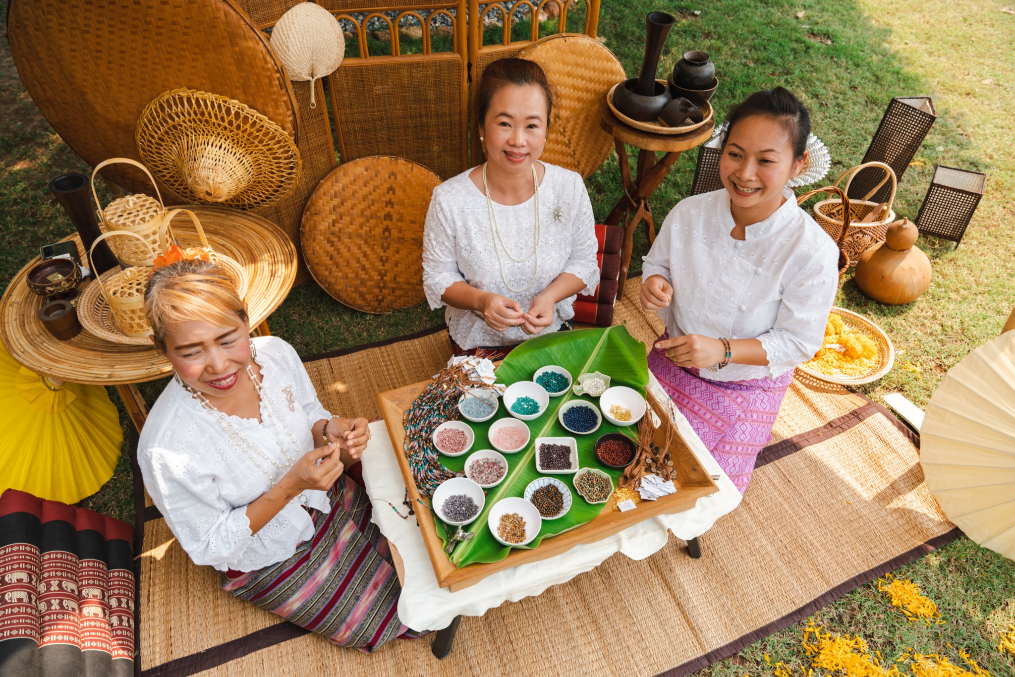 Three women in white tops sit at a table outdoors with tea and snacks, smiling and enjoying a gathering.