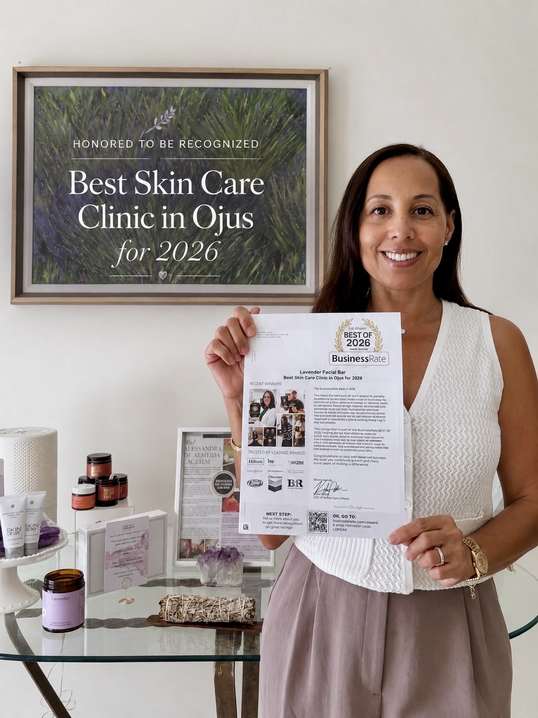 Woman holding a newspaper in a clinic, smiling, with a framed award on the wall behind her.