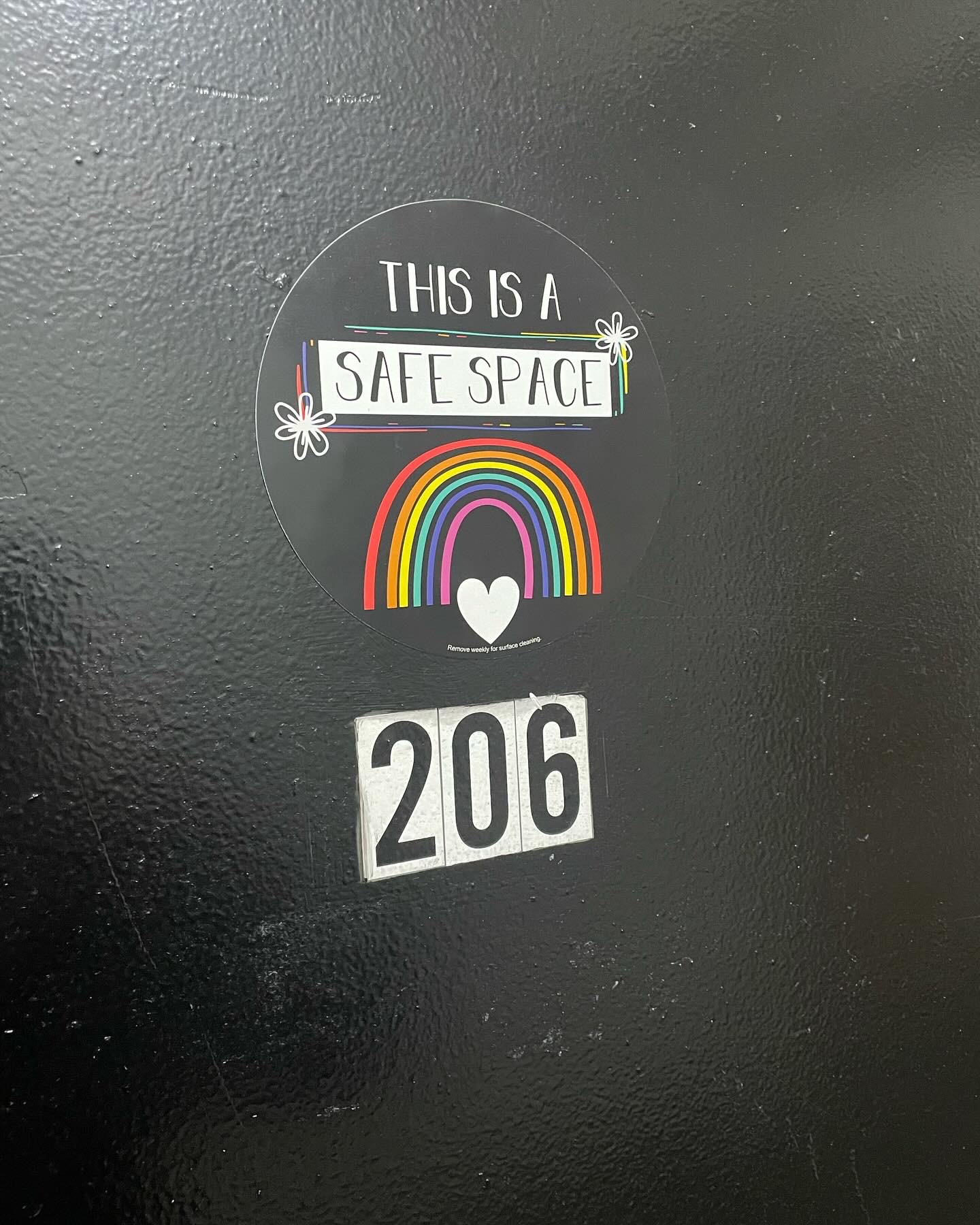 Sticker with text 'This is a safe space', rainbow, heart, and butterflies on a black surface.