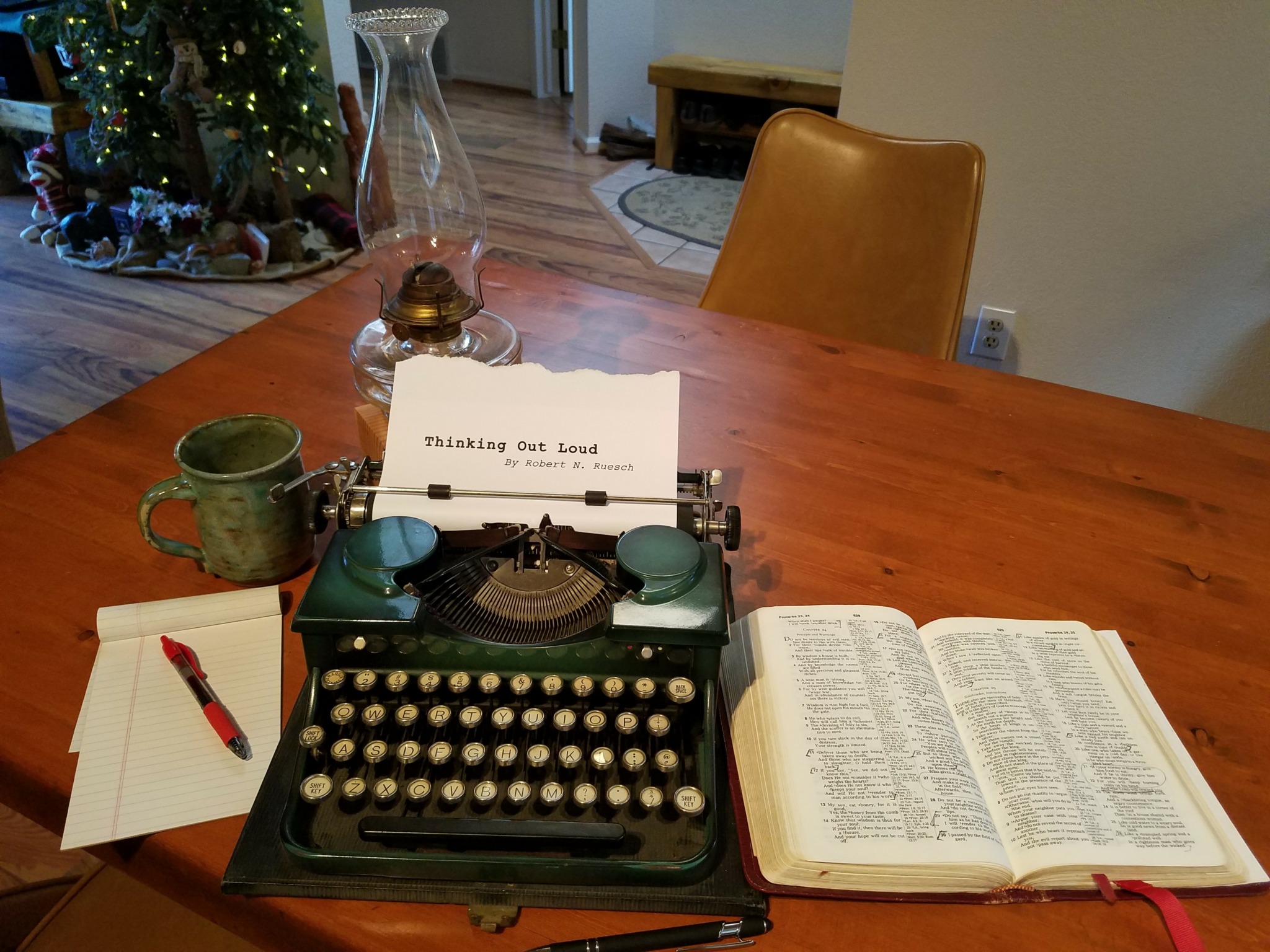 Typewriter with a paper reading 'Thinking out Loud', open book, mug, and notepad with pen on wooden table.
