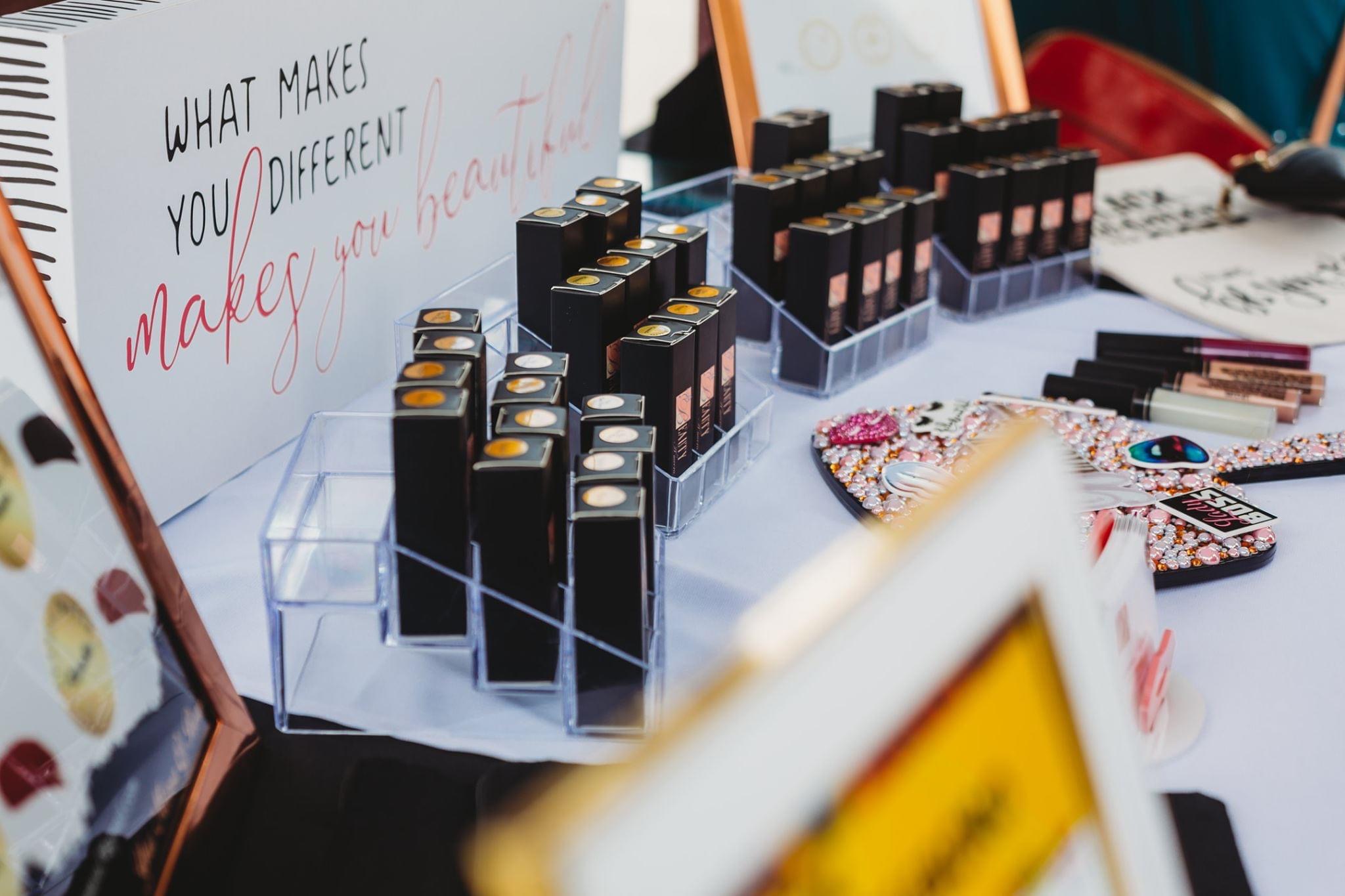 Display of makeup lipsticks and accessories on a table with a sign in the background.