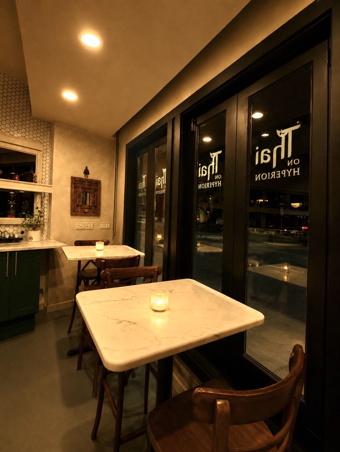 Interior of a cozy cafe with a table near large glass windows, warm lighting, and a candle on the table.