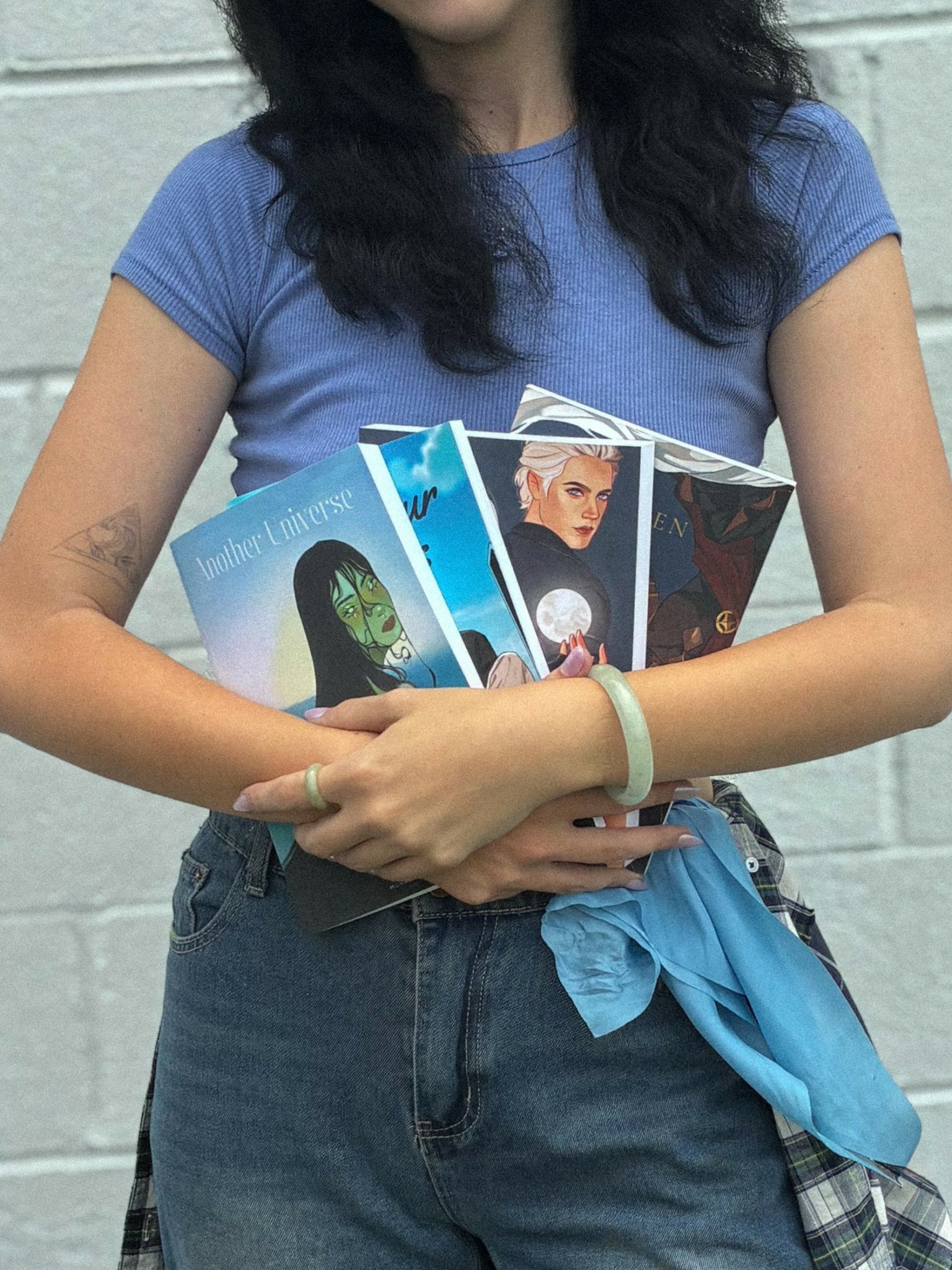 Person holding several cards or photographs, wearing a blue t-shirt and jeans, with a brick wall background.
