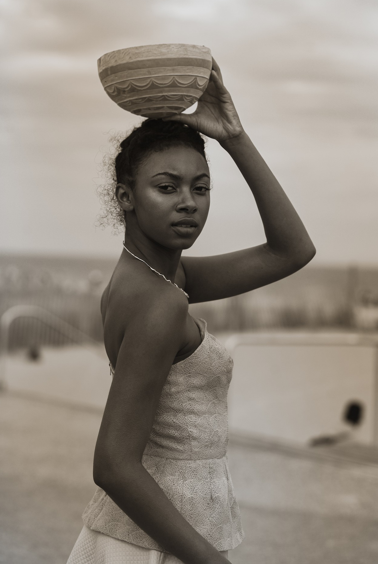 Young woman with a bowl on her head, standing outdoors, looking at the camera, in black and white.