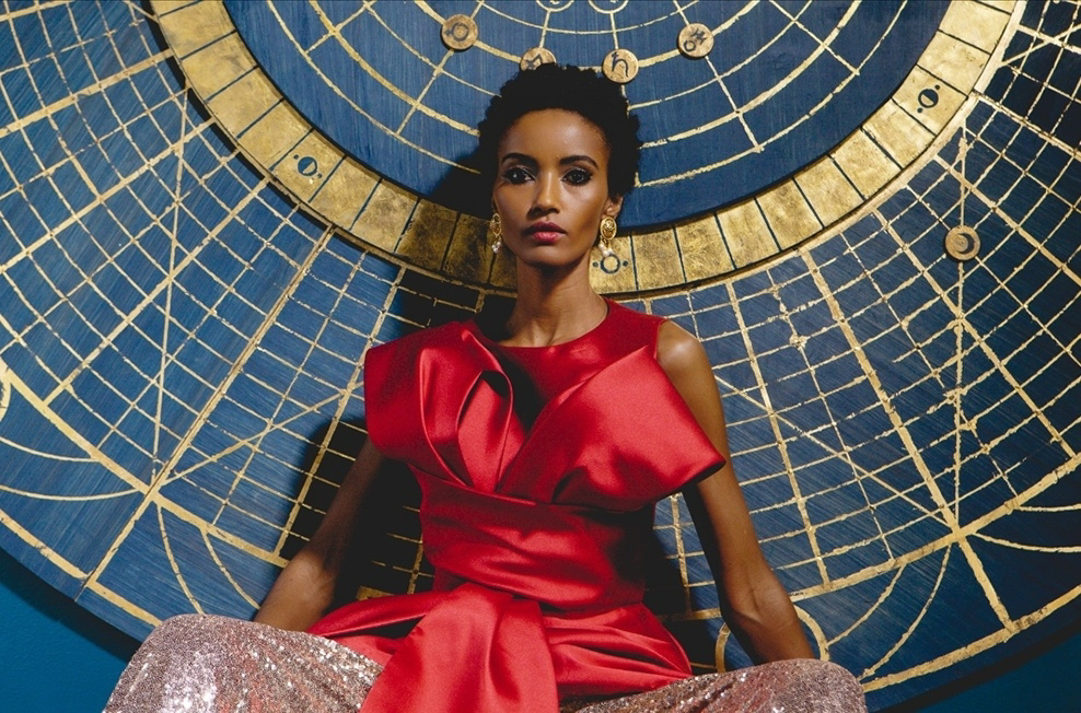 Woman in red dress sitting in front of a large, intricate gold and blue circular design background.