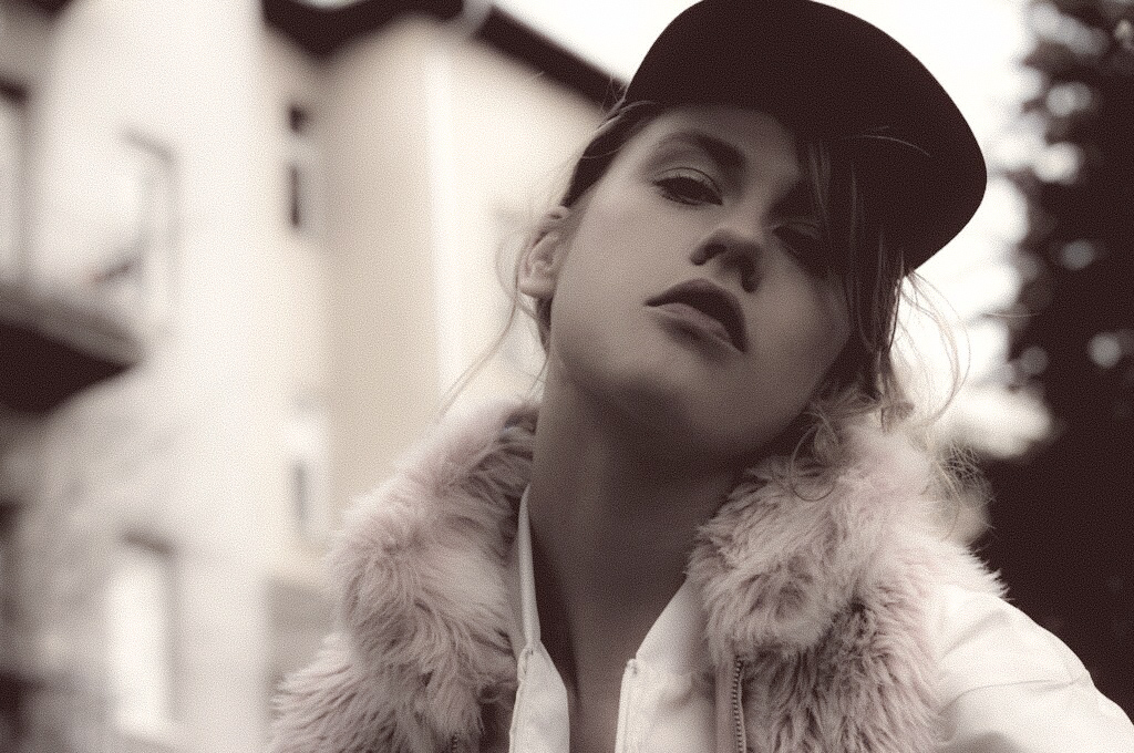 Portrait of a woman wearing a cap and fur coat outdoors, with a serious expression, in black and white.