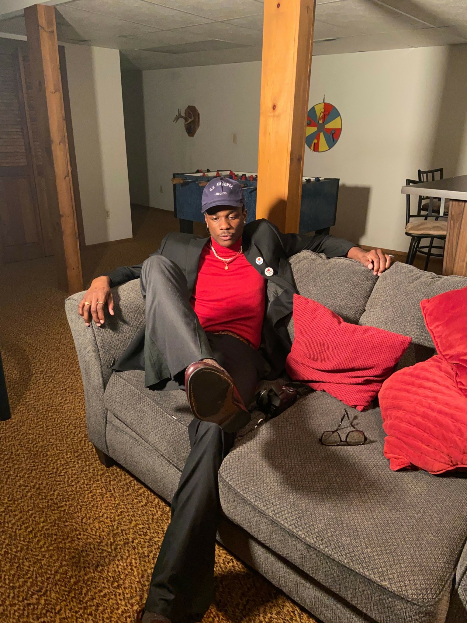 Person sitting on a gray couch with red and gray blankets, holding a phone, in a living room.