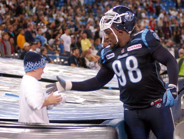 Football player in uniform high-fives a young fan wearing a beanie, with a crowd in the background.
