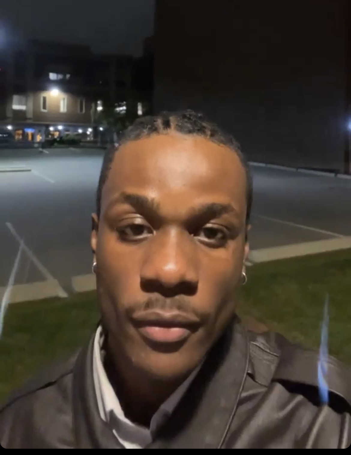 Young man with braided hair and earrings outdoors at night, illuminated by streetlights.