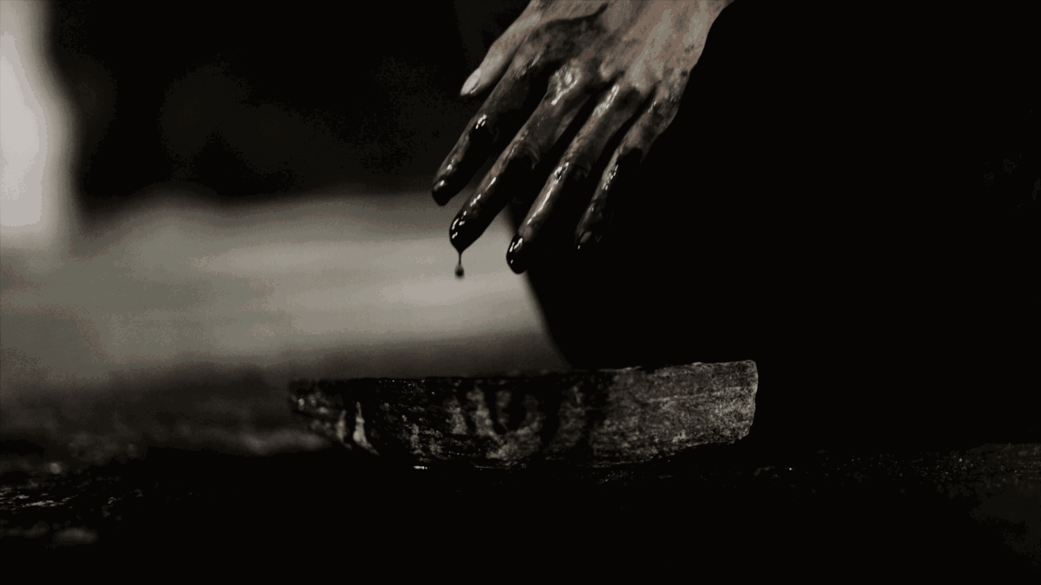 Close-up of a person's hand dripping water over a flat surface, with a dark background.