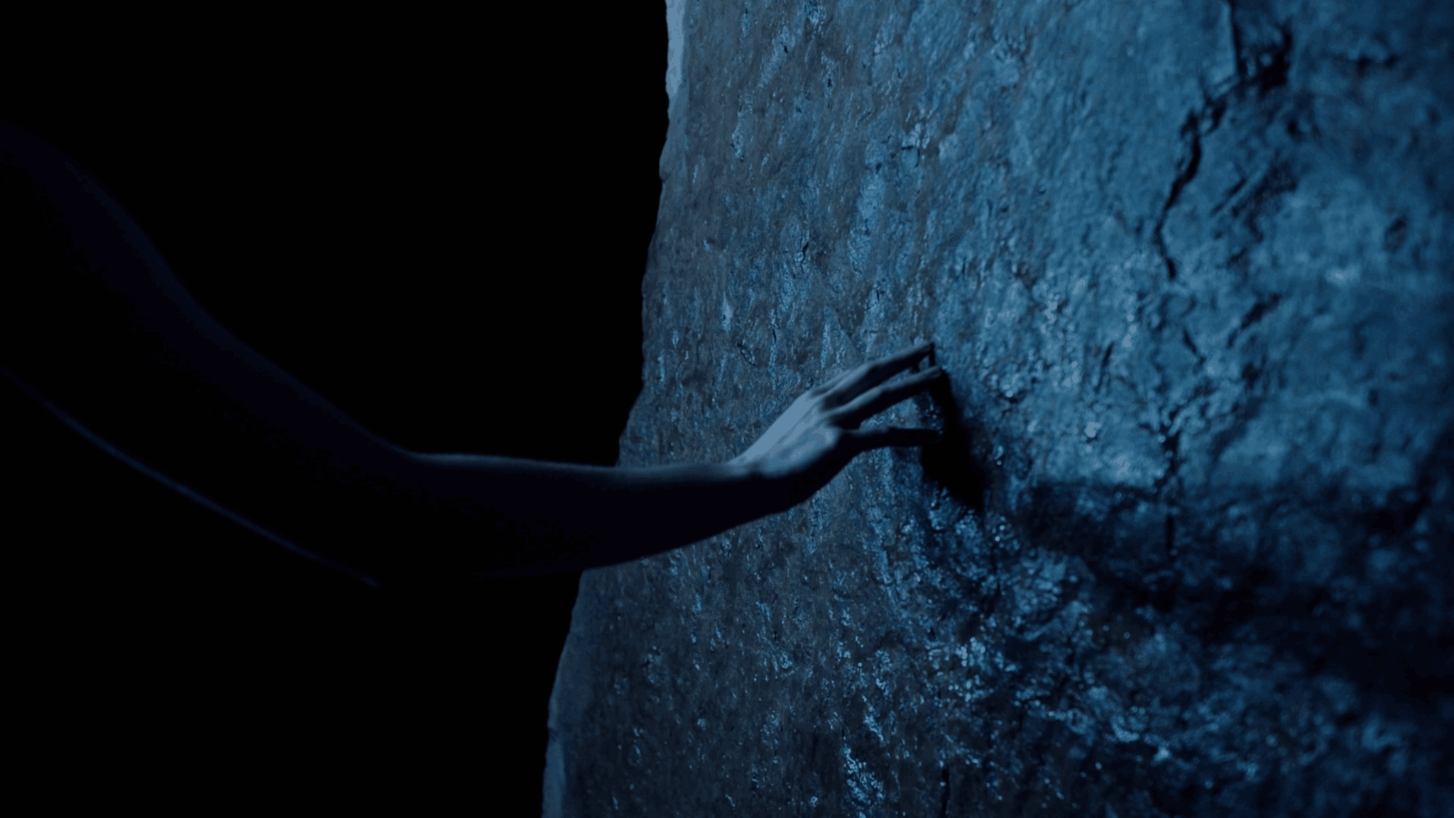 Person's hand touching a textured rock surface in a dark environment.