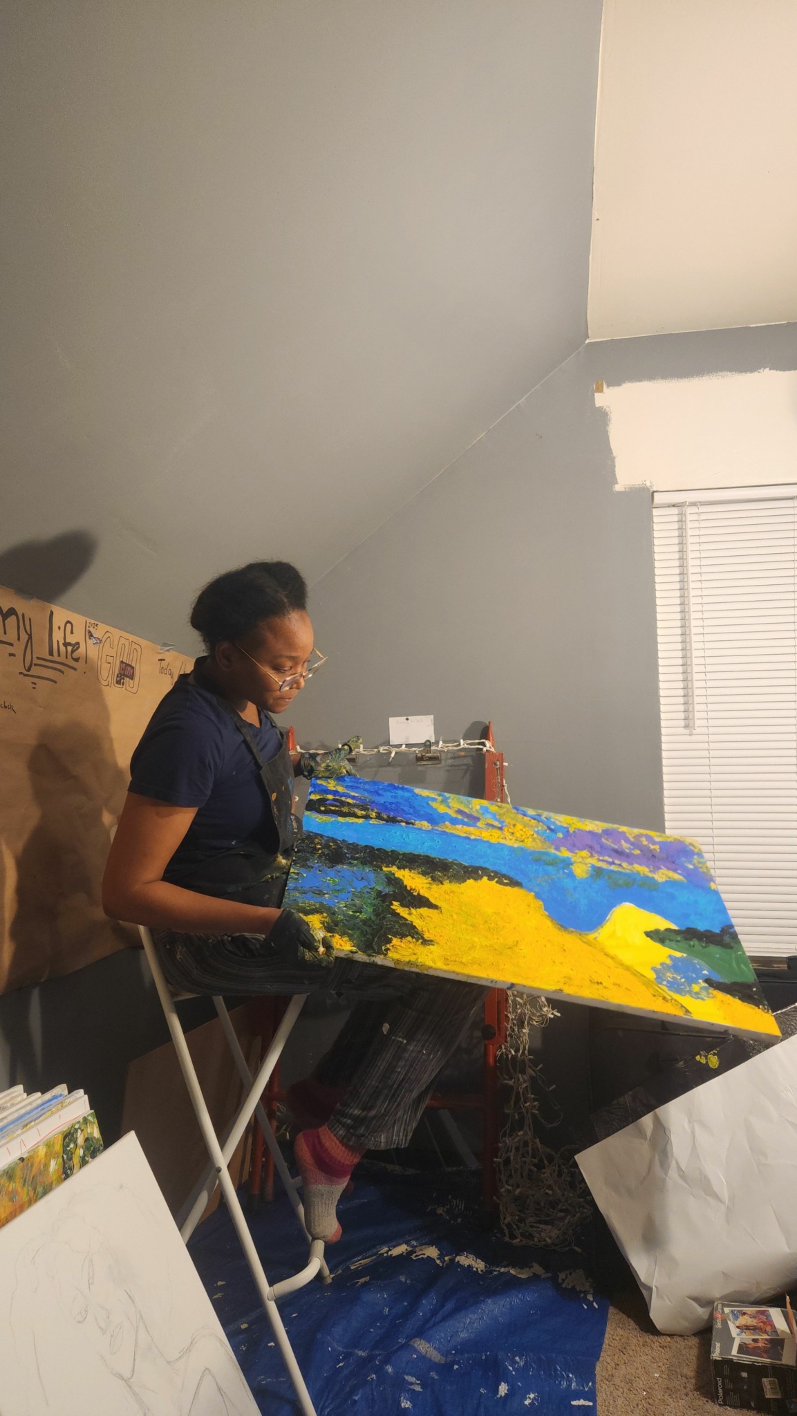 Person painting a colorful landscape on a canvas in a room with gray walls.