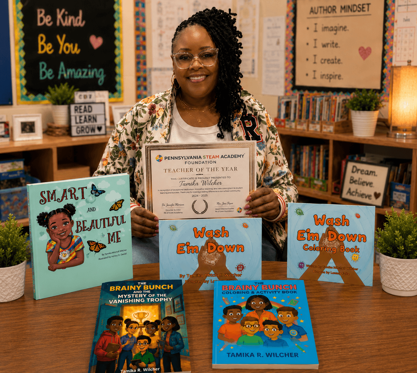 Smiling woman holding a certificate in a classroom with books and motivational posters, surrounded by children's books on a table.