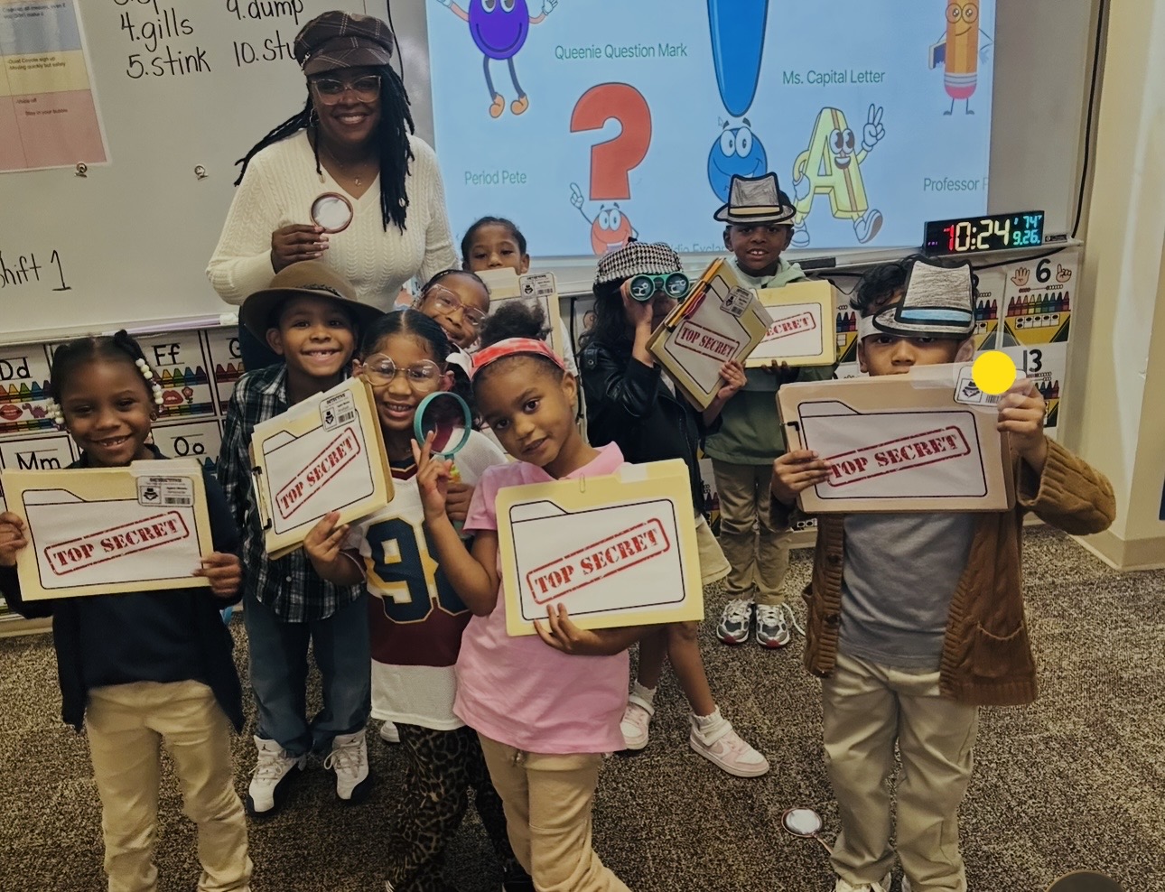 Group of children and a teacher in a classroom holding signs that say 'Top Secret.'