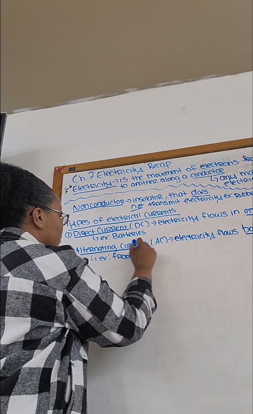 Person writing on a whiteboard with notes and diagrams, wearing a checkered shirt, in a classroom or meeting room.