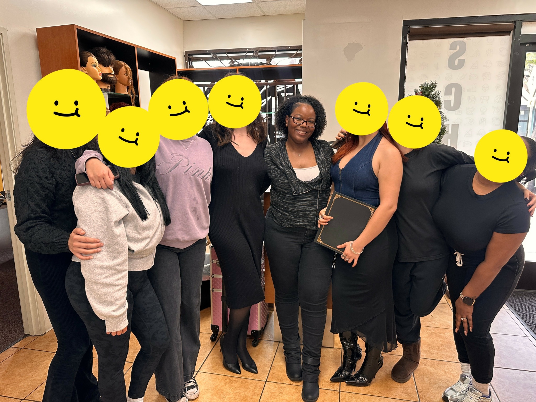 Group of seven people standing indoors, some holding folders, with faces covered by yellow smiley faces.