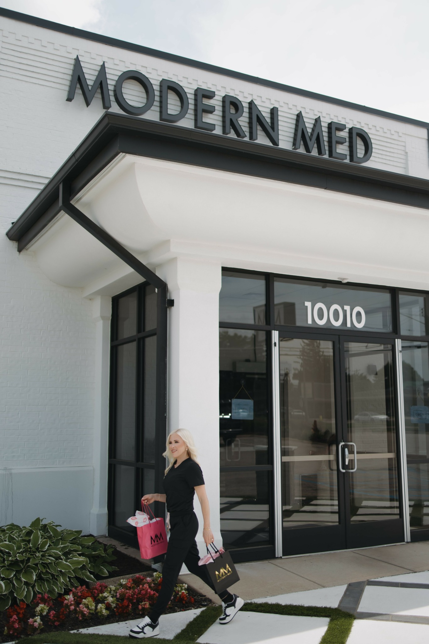 Person walking outside a building with a sign reading 'MODERN MED' above the entrance, holding a pink bag and a black bag.