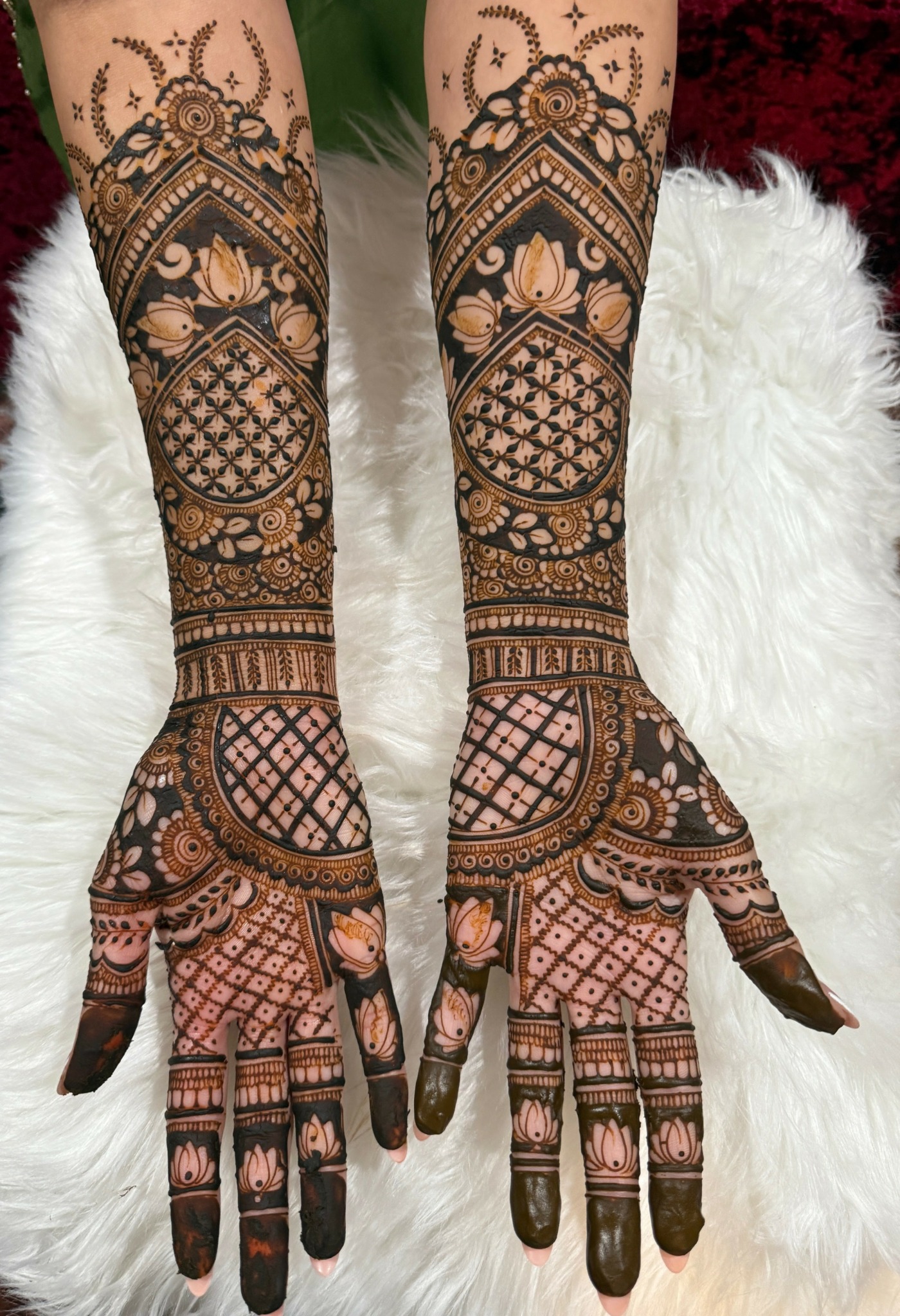 Two hands with intricate henna designs resting on a white furry surface, detailed patterns cover fingers and wrists.