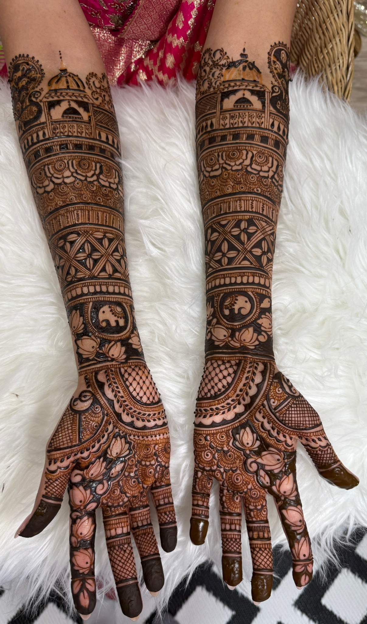 Two arms with intricate henna designs extending from hands to upper arms, resting on a white furry surface.