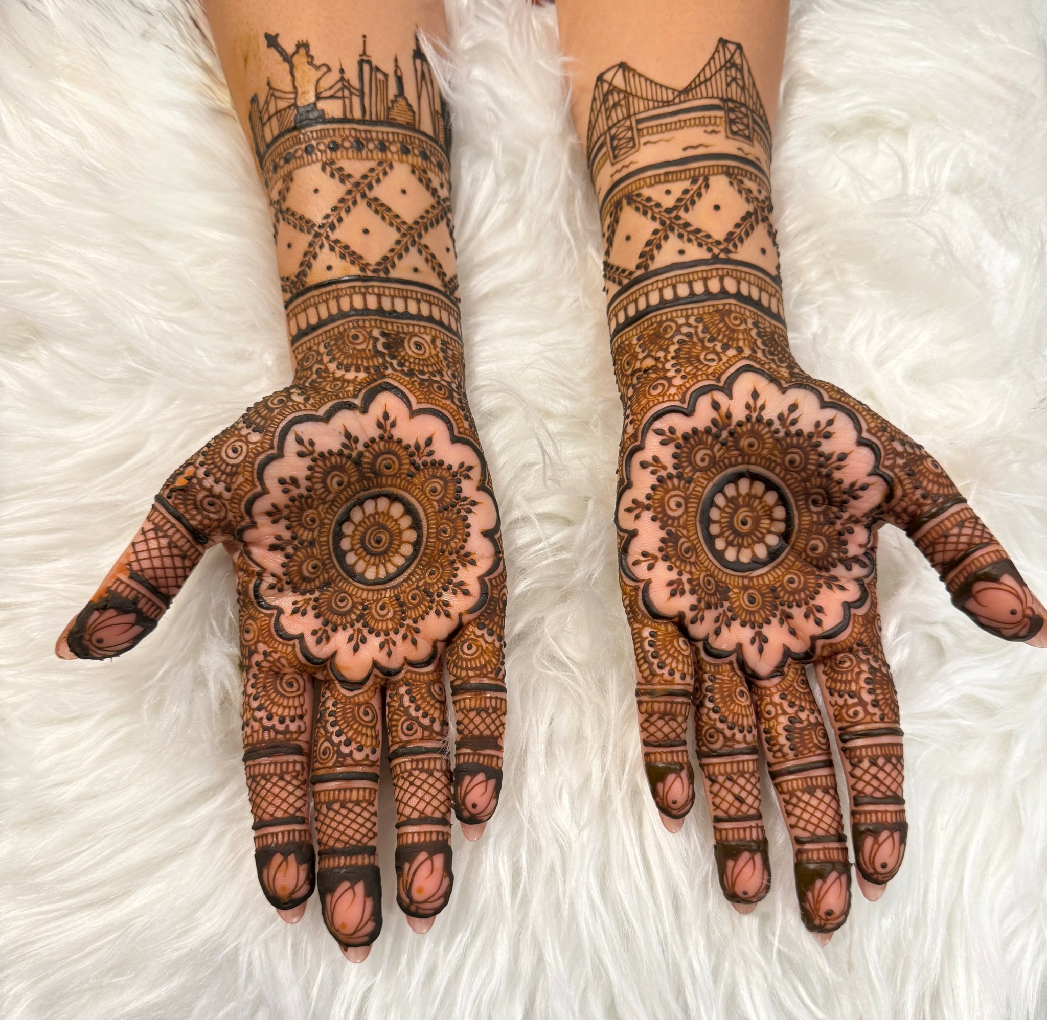 Two hands with intricate henna designs resting on a white furry surface, showing detailed patterns on palms and fingers.