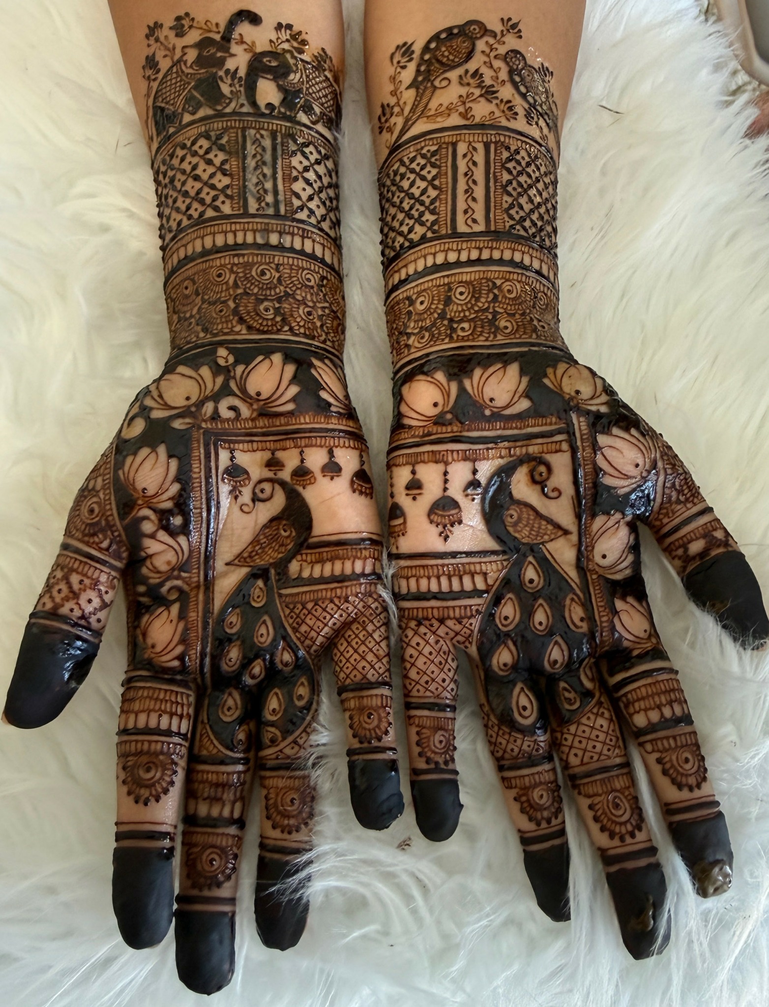 Person's hands and forearms with intricate henna designs, resting on a white furry surface.