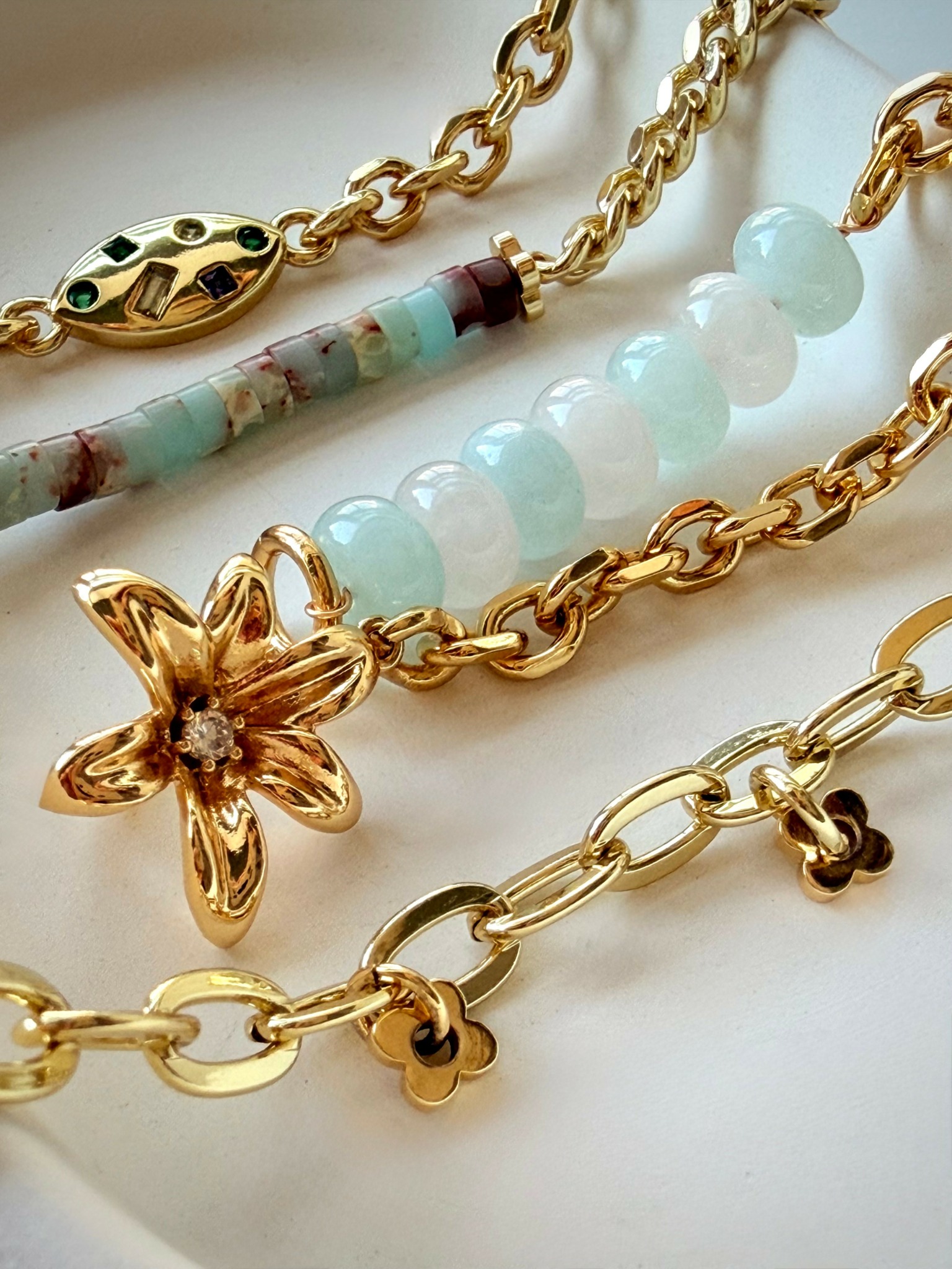 Close-up of gold jewelry with flower and bead designs, including chains and a star-shaped pendant.
