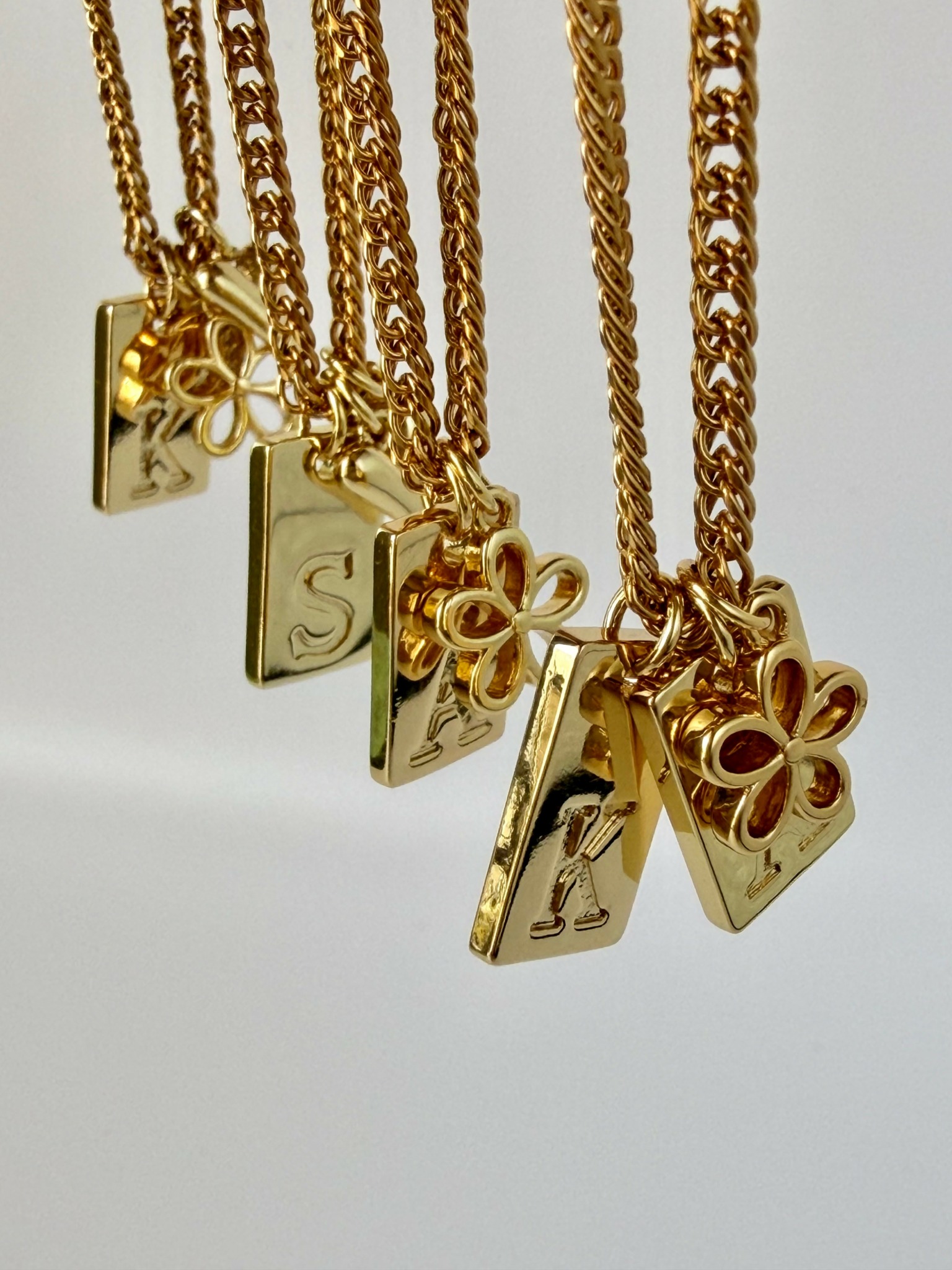 Gold necklaces with various pendant charms hanging against a white background.