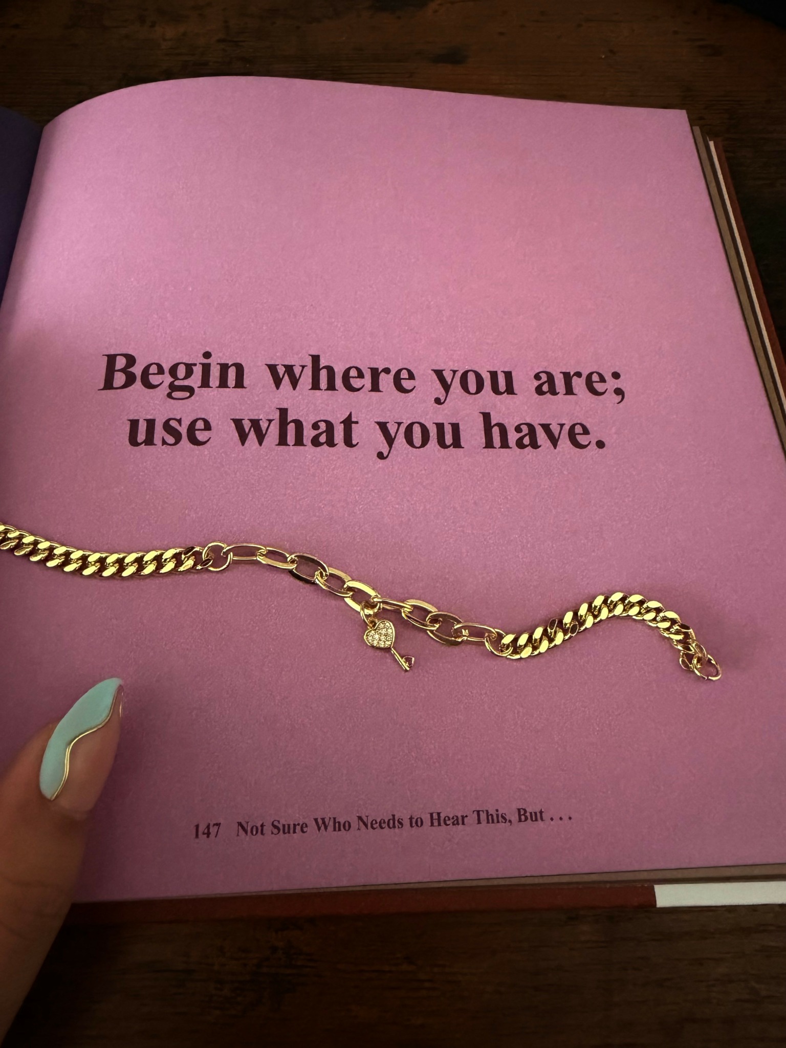 Pink page with black text reading, 'Begin where you are; use what you have.' A gold chain bracelet is placed on the page.