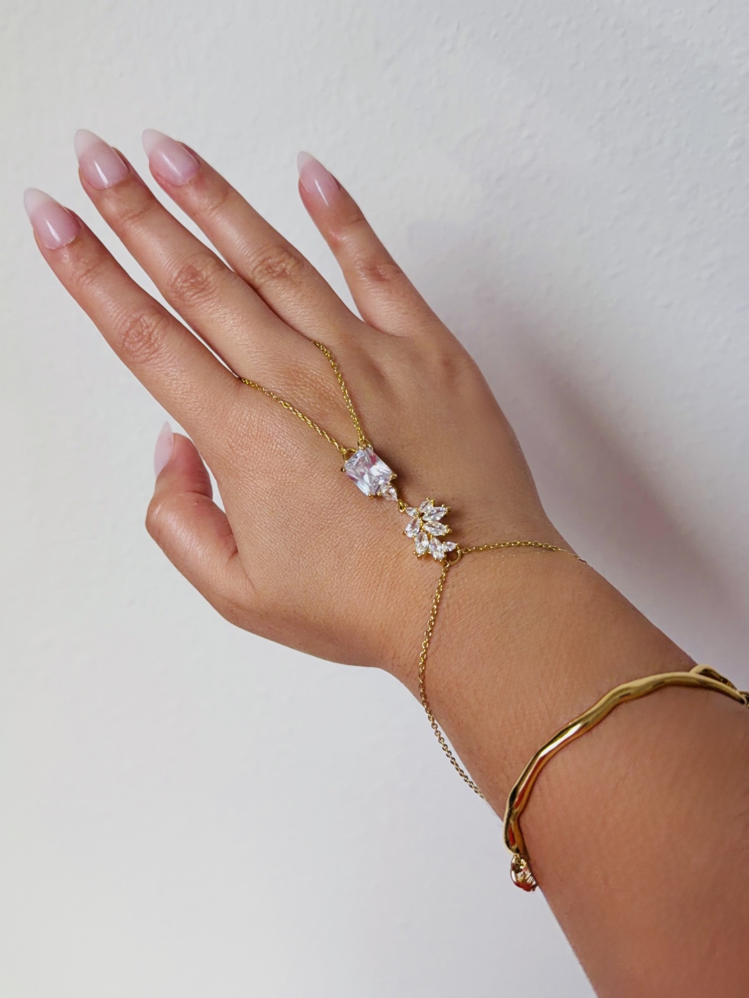 Hand with rings and bracelets against a plain background, showing jewelry on fingers and wrist.