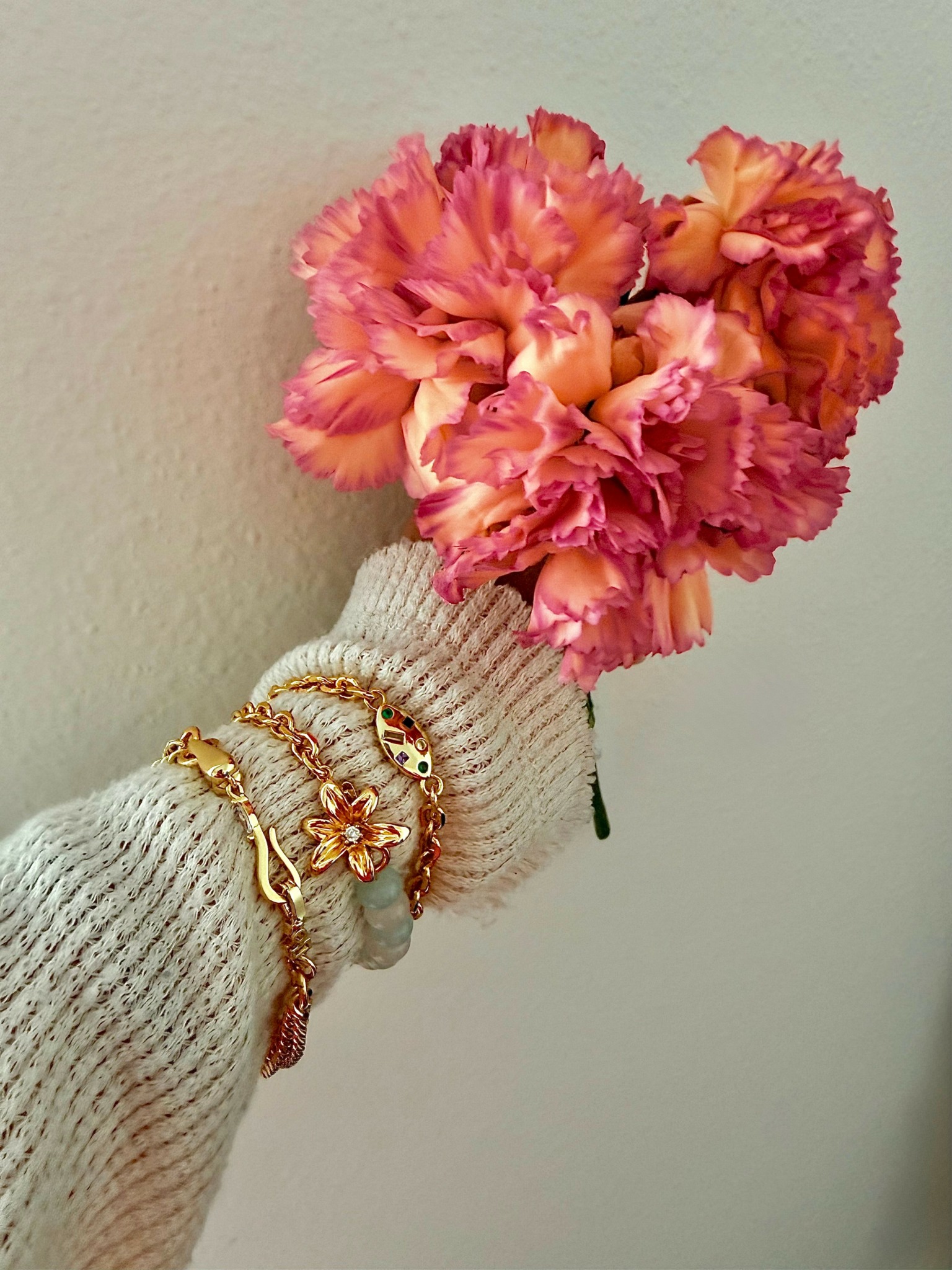 Person wearing a beige sweater holding a bouquet of pink and orange carnations against a plain background.