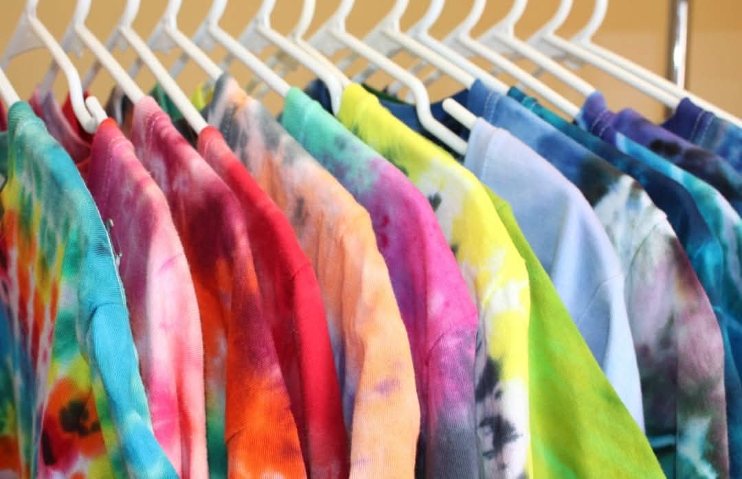 Colorful tie-dye shirts hanging on a rack, arranged in a row with various bright colors and patterns.