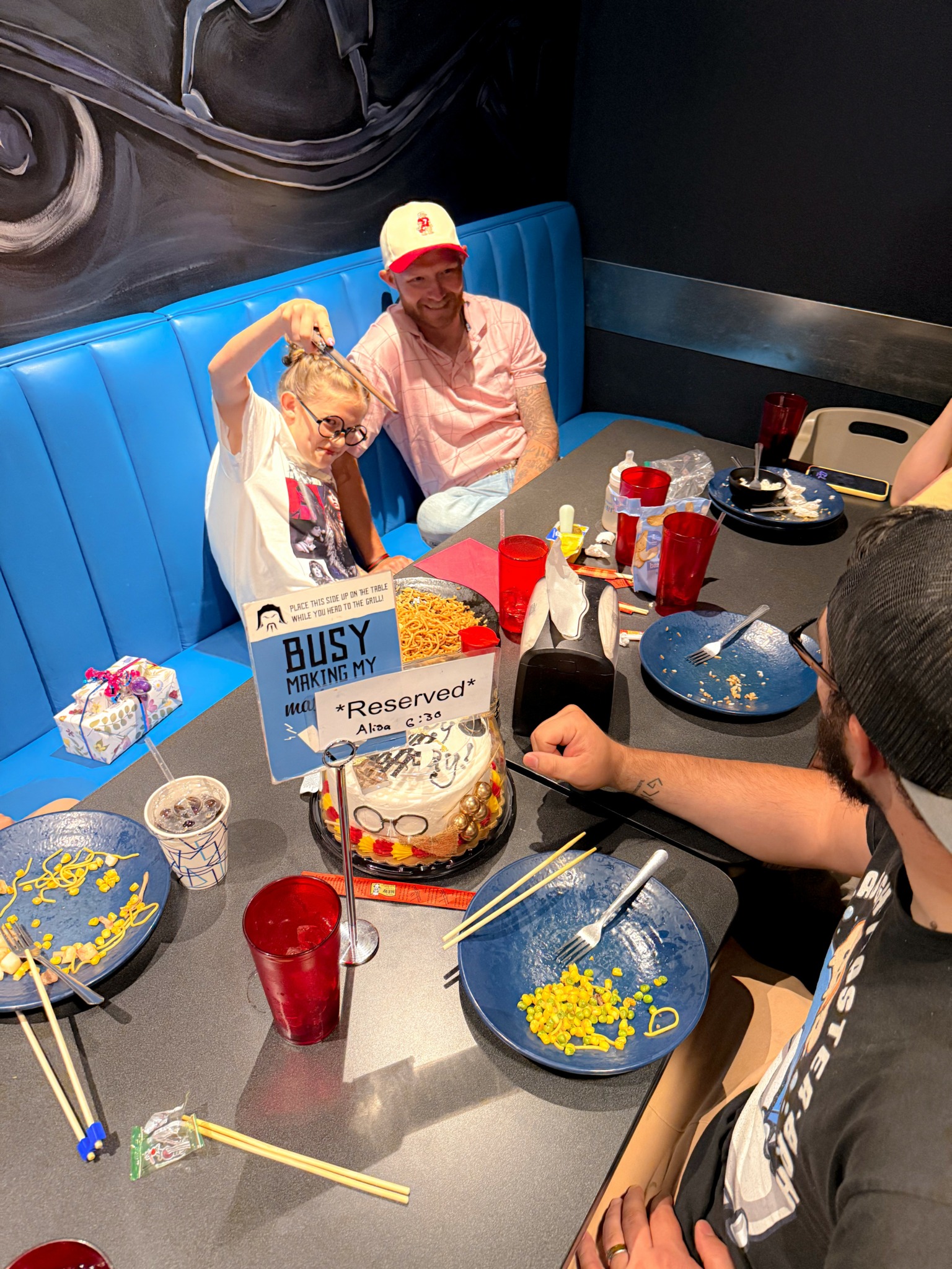 People sitting at a table with birthday cake, drinks, and party decorations, celebrating a birthday in a restaurant.