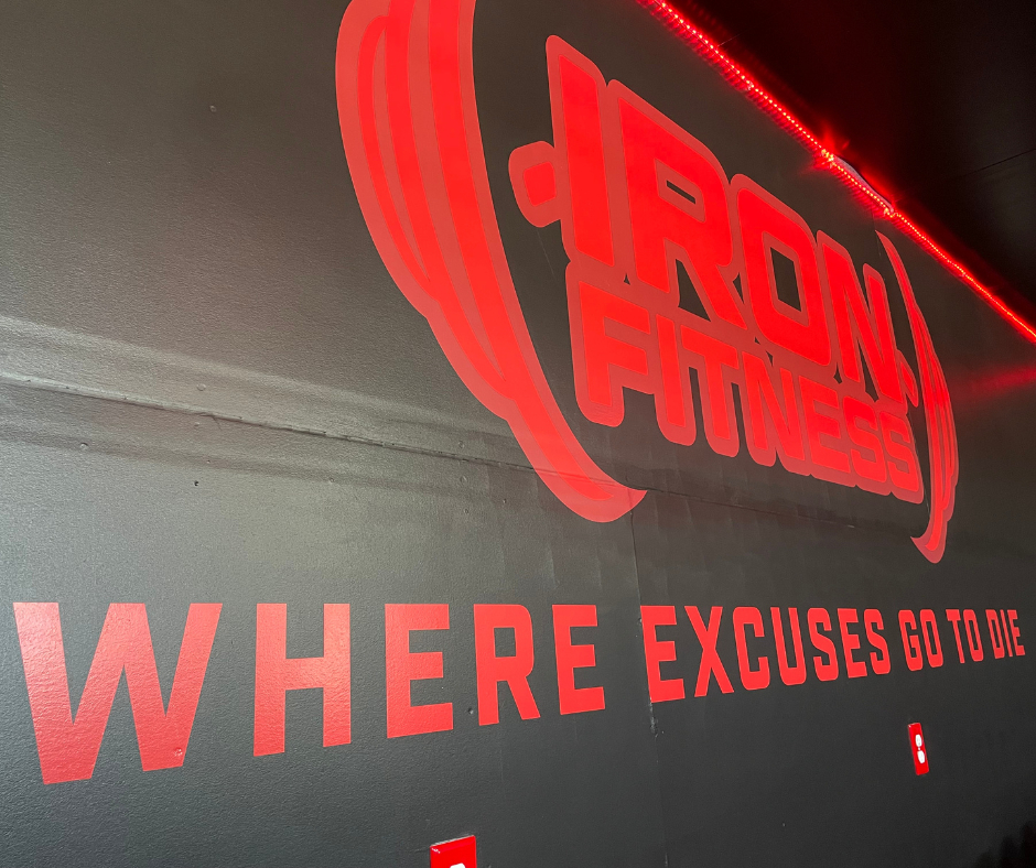 Red illuminated sign with the words 'IRON ATTACK' and a slogan 'WHERE EXCUSES GO TO DIE' on a gray wall.