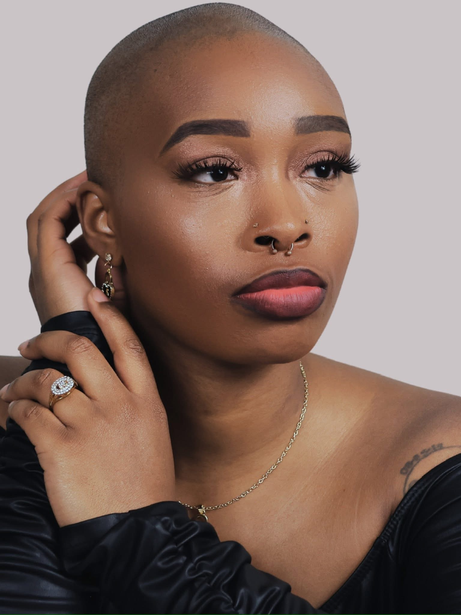 Portrait of a woman with a shaved head, wearing jewelry, and looking to the side.
