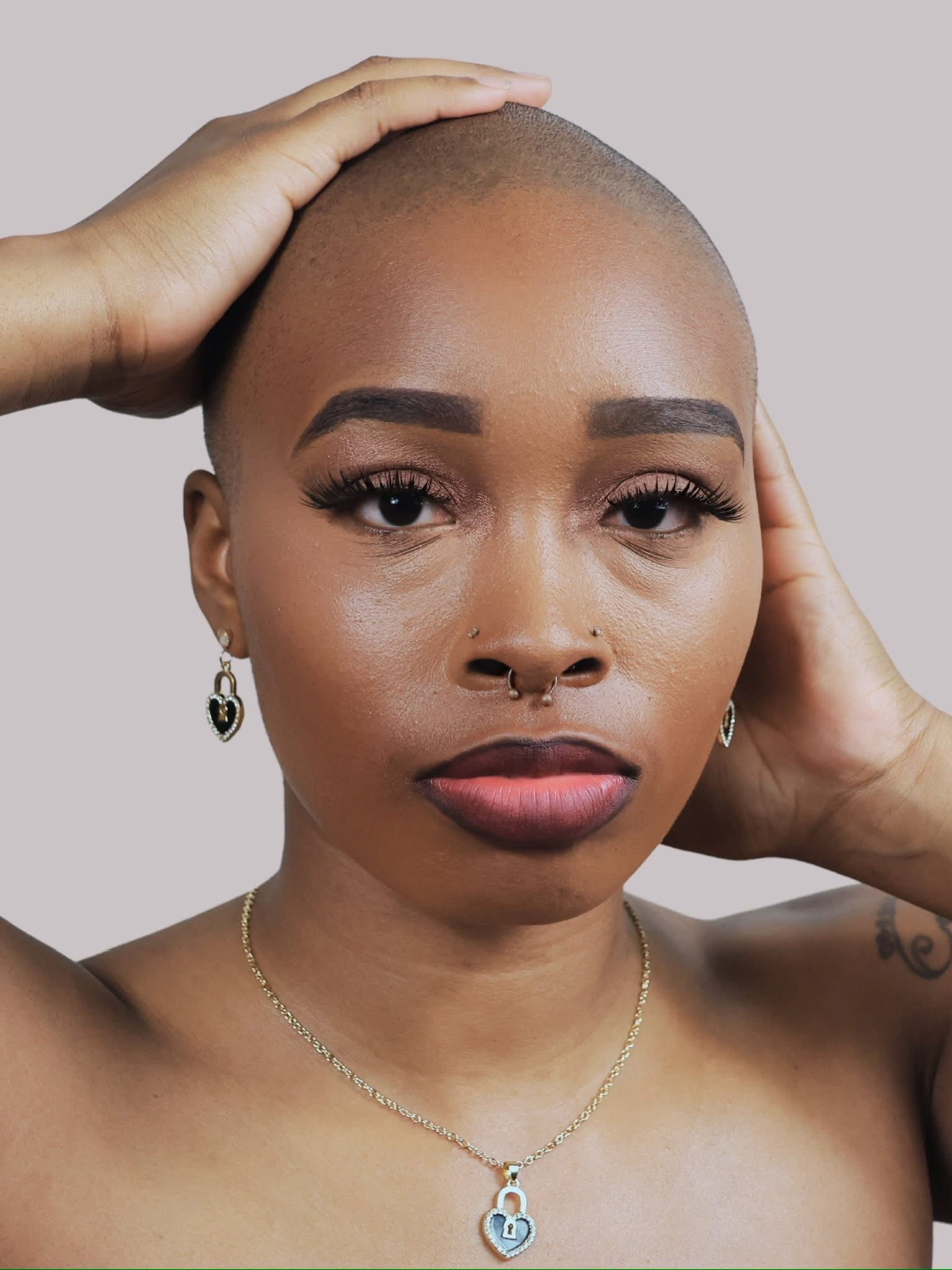 Close-up of a woman with a shaved head, wearing earrings and a necklace, looking directly at the camera.