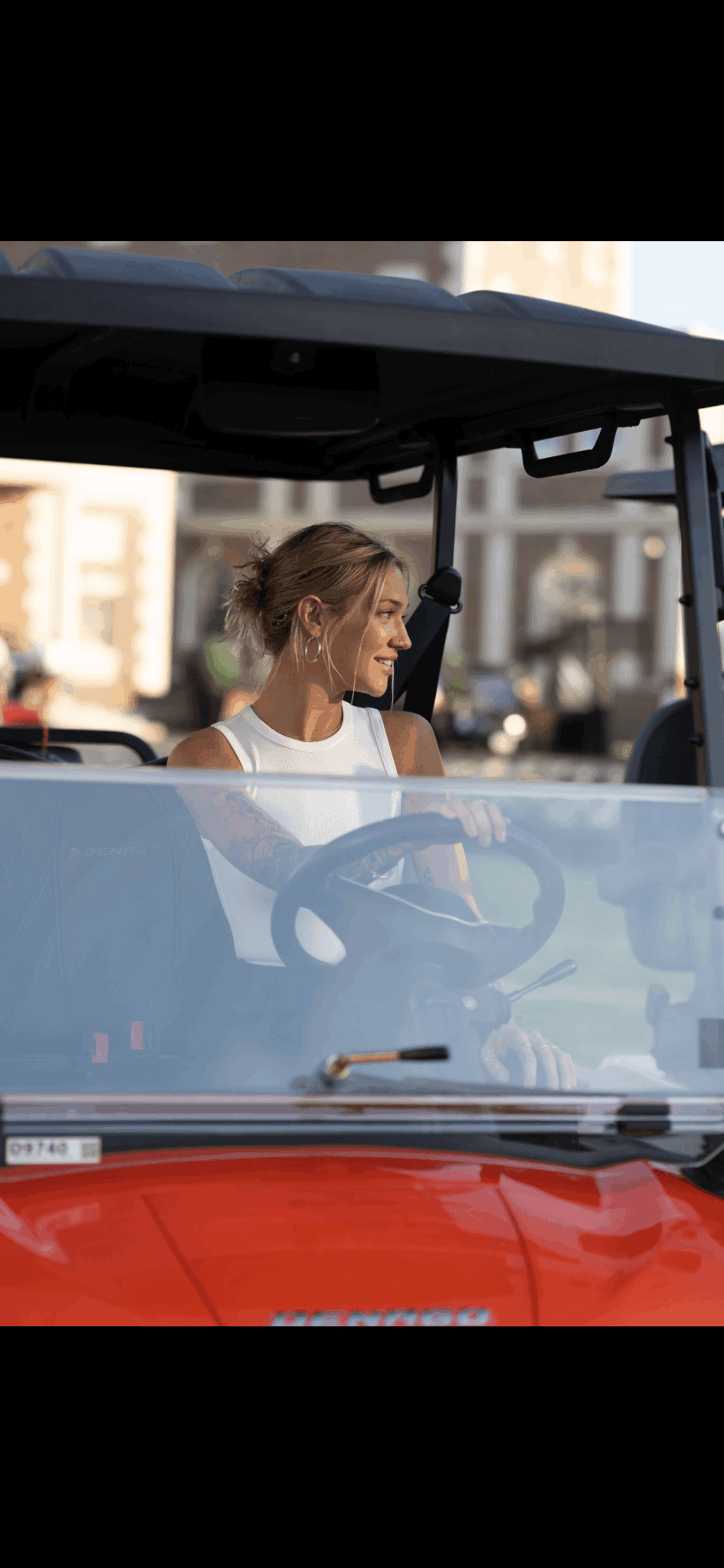 Woman sitting in a vehicle, looking to the side, with a city street background.
