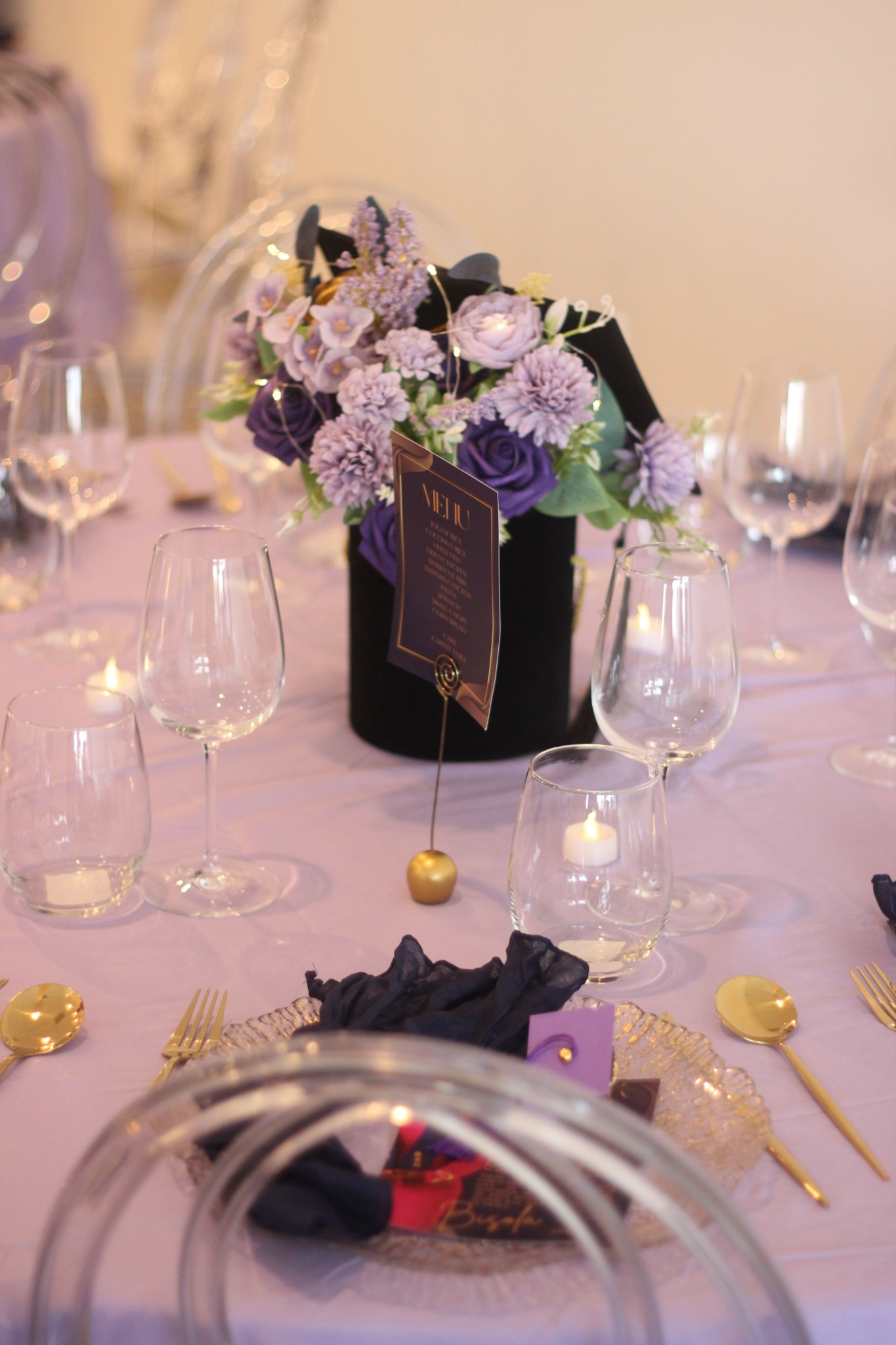 Table setting with glassware, a black box with a card, and a floral arrangement with purple and white flowers.
