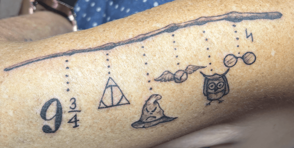 Tattoo of a dotted line, a sailboat, a frog, a camera, and a pair of glasses on a person's arm.