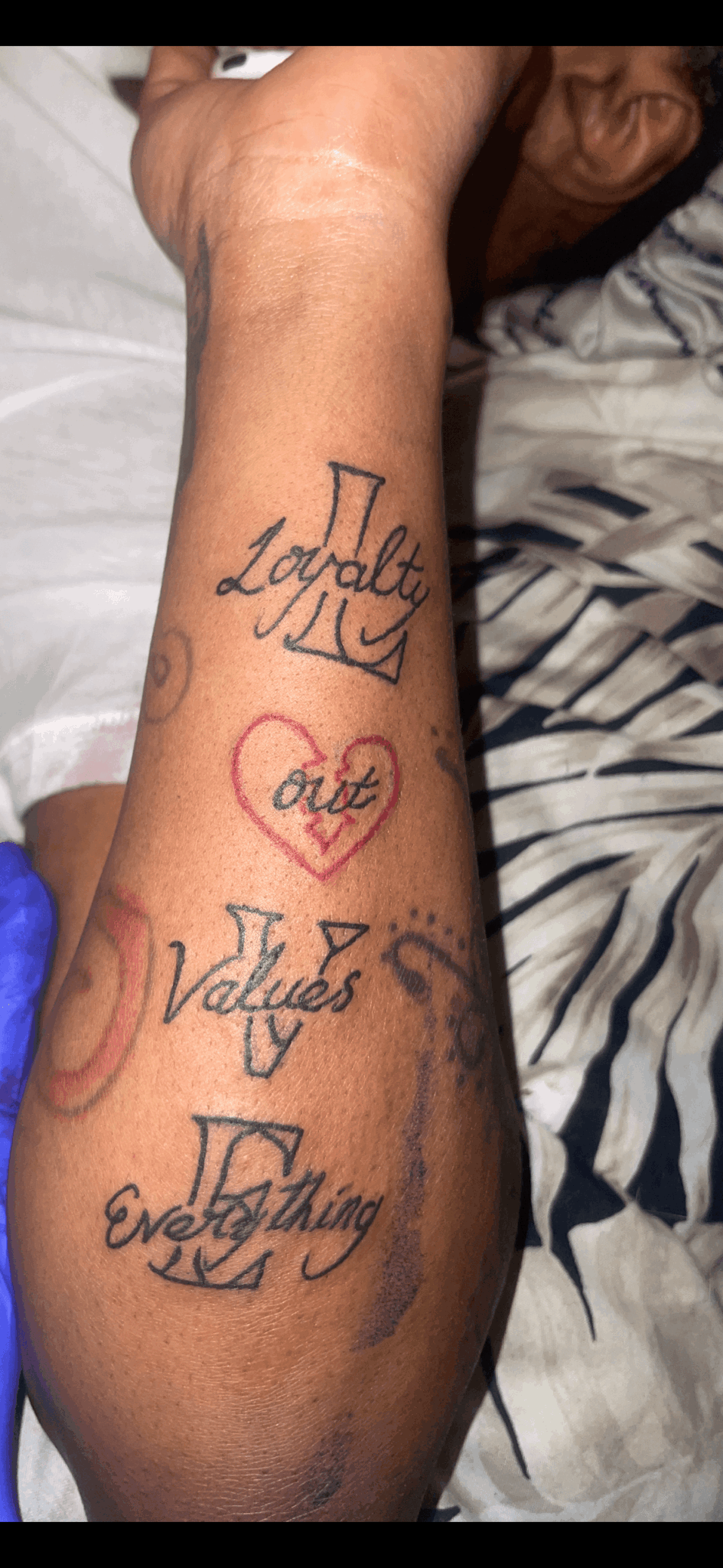 Forearm with tattooed words and a heart with the word 'Love' inside, lying on a bed.