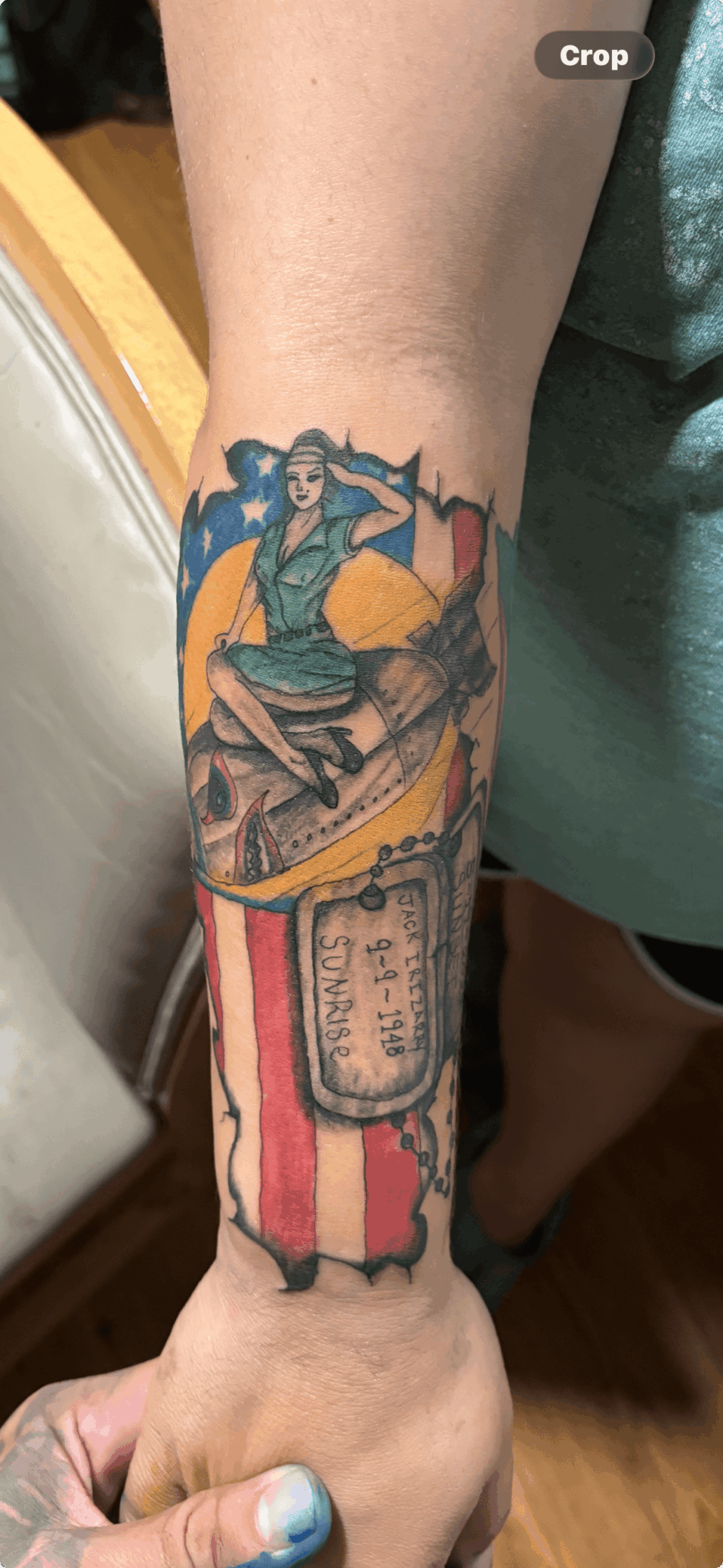 Colorful tattoo of a woman riding a broomstick over a sunset, with a scroll and decorative elements on the forearm.