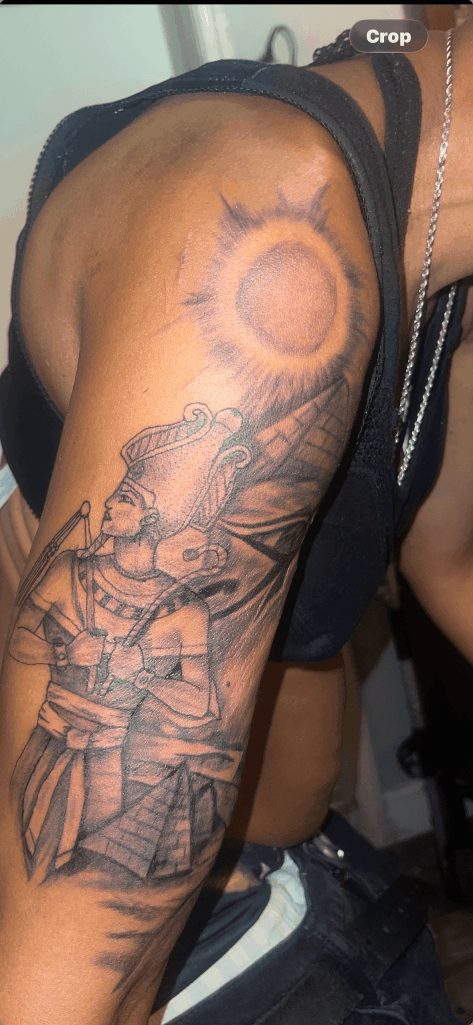 Tattoo of a warrior with a sword on upper arm, sun above, and mountain background, in black and gray ink.