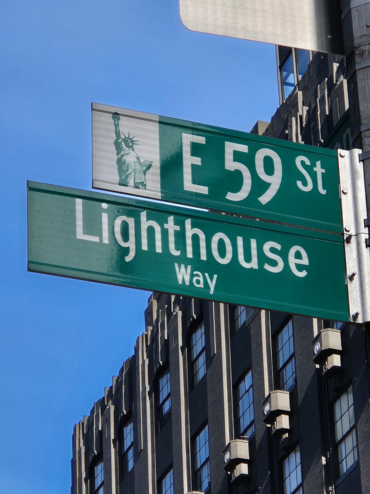 Street signs for E 59th Street and Lighthouse Way against a building and blue sky