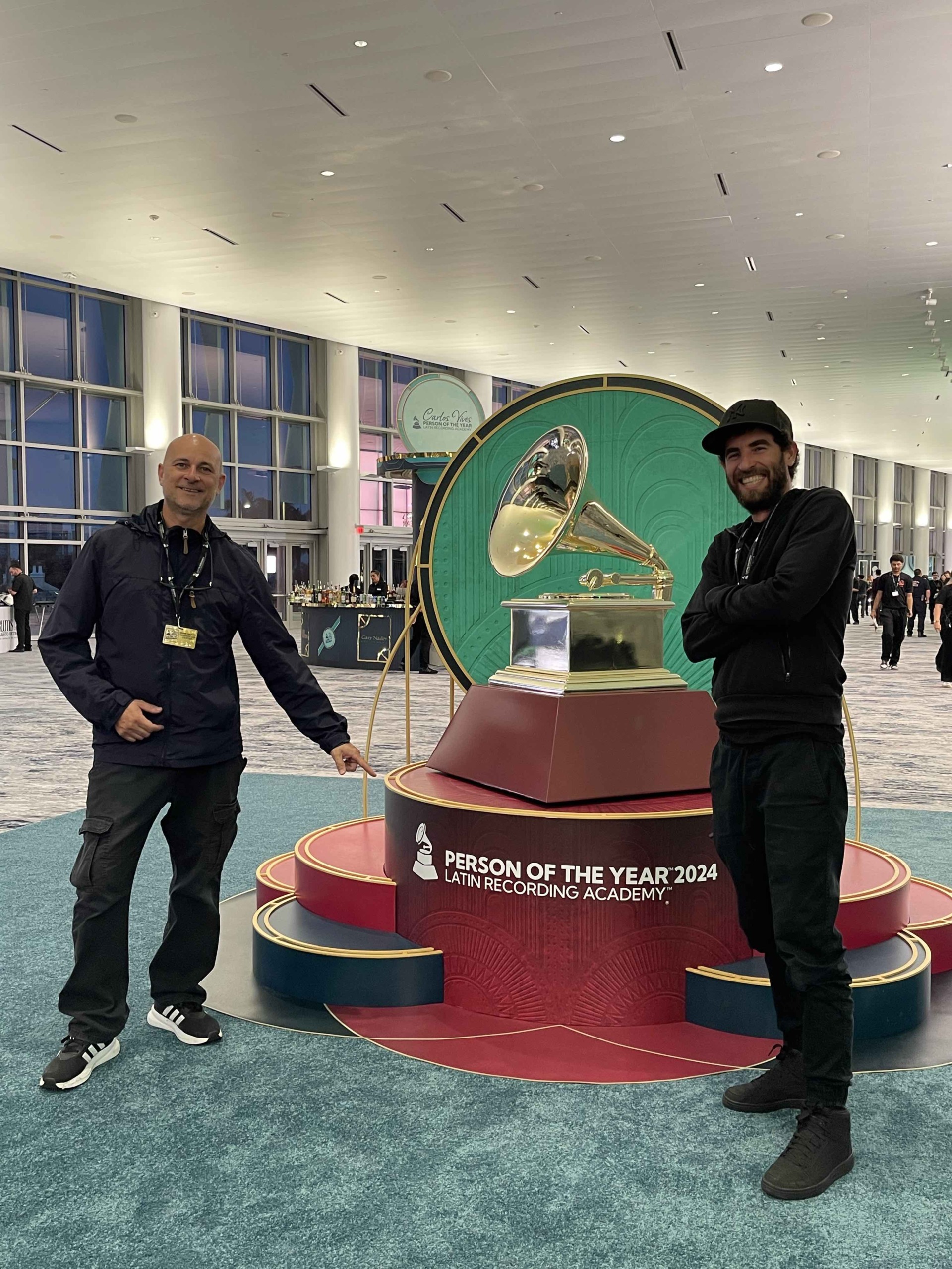 Two men stand beside a large Grammy award display at an event, with a sign reading 'Person of the Year 2024.'
