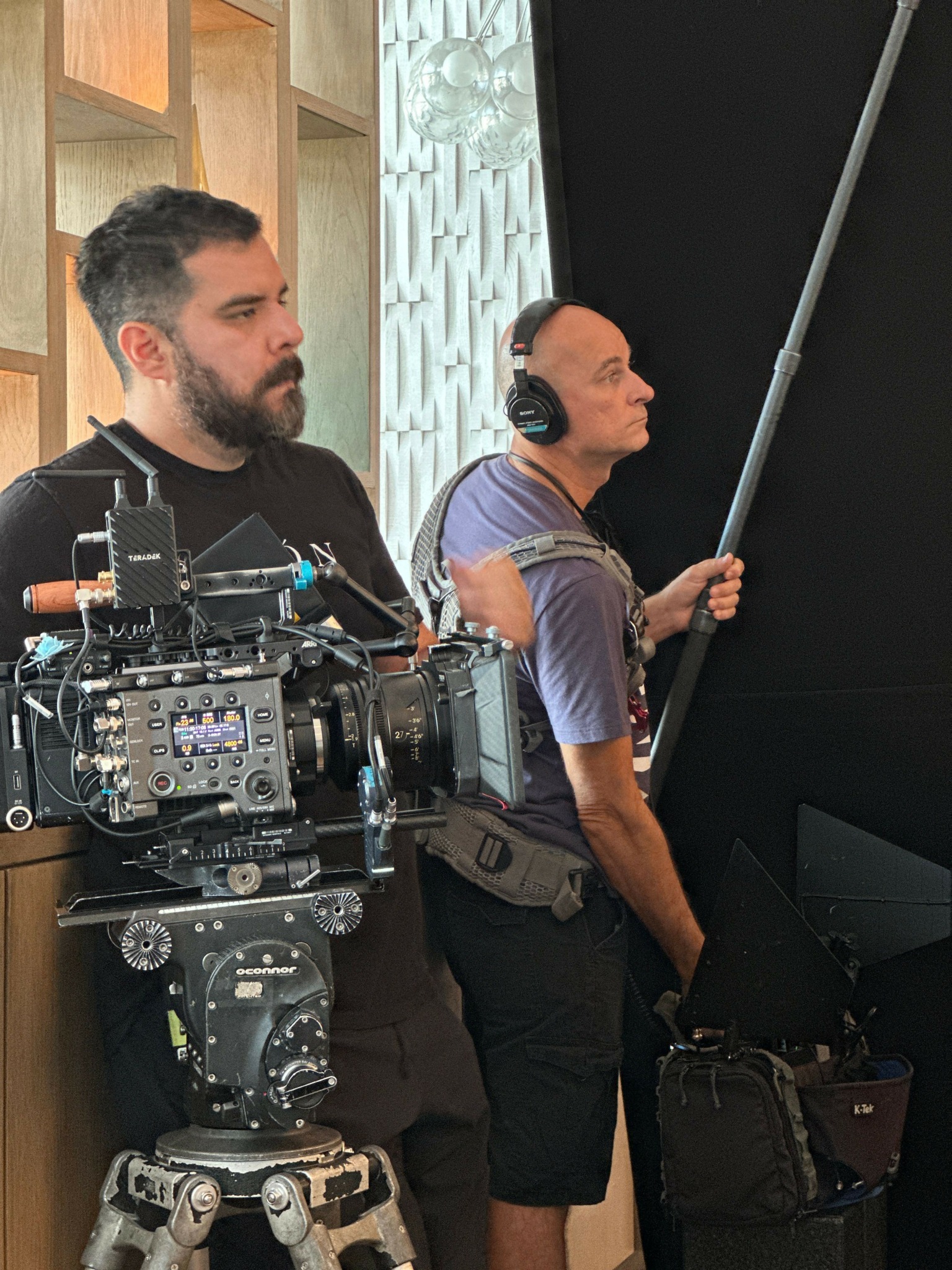 Two men working with a professional camera setup in a studio, one holding a boom microphone, the other operating the camera.
